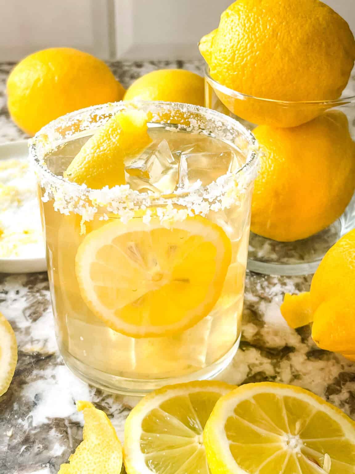 Lemon margarita with salted rim and lemon wedge over ice.