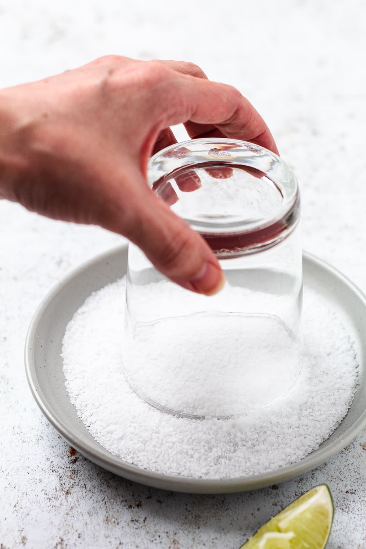 Step-by-step image of salting a margarita glass rim using coarse salt and a lime wedge.