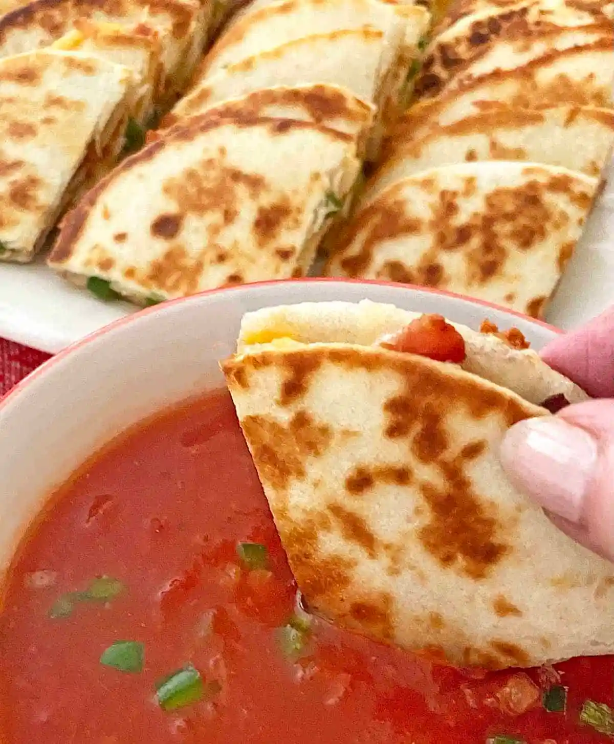 Mini quesadilla dipped into salsa with crispy browned tortilla and melted cheese.