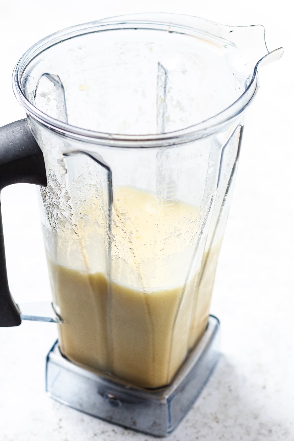 Blender container filled with a light yellow blended mixture on a light surface.