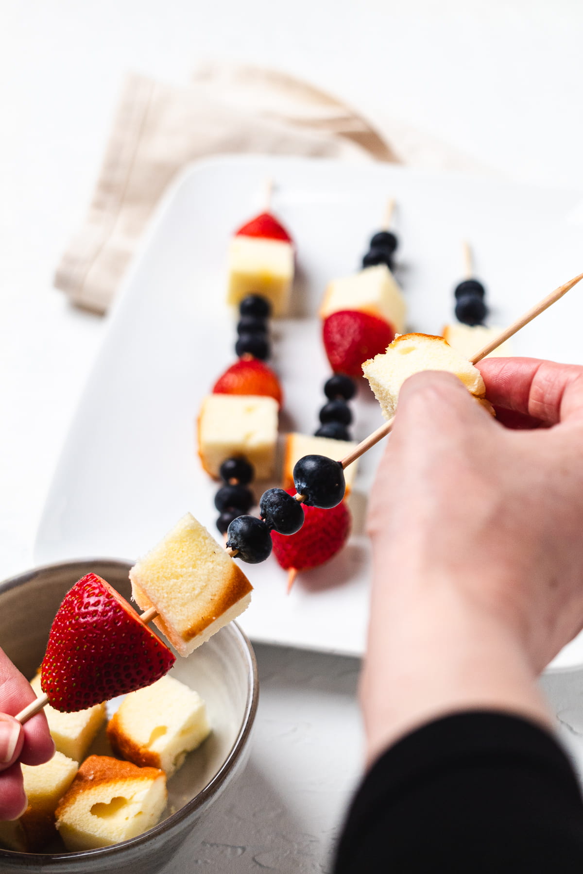 Hand adding pound cake to a skewer with berries.
