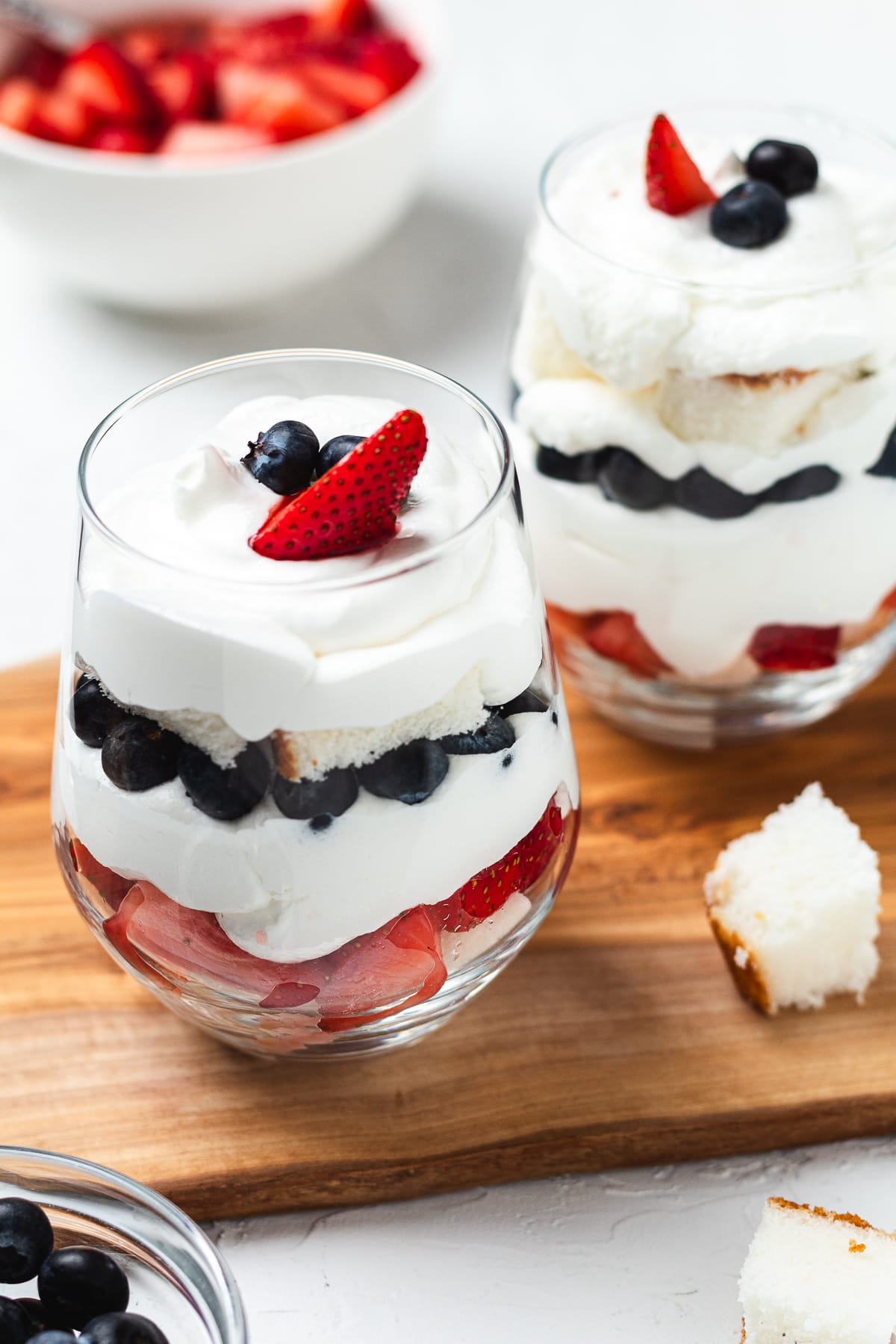 Red, white, and blue berry trifles with cake and whipped cream in glass cups on a wooden board.