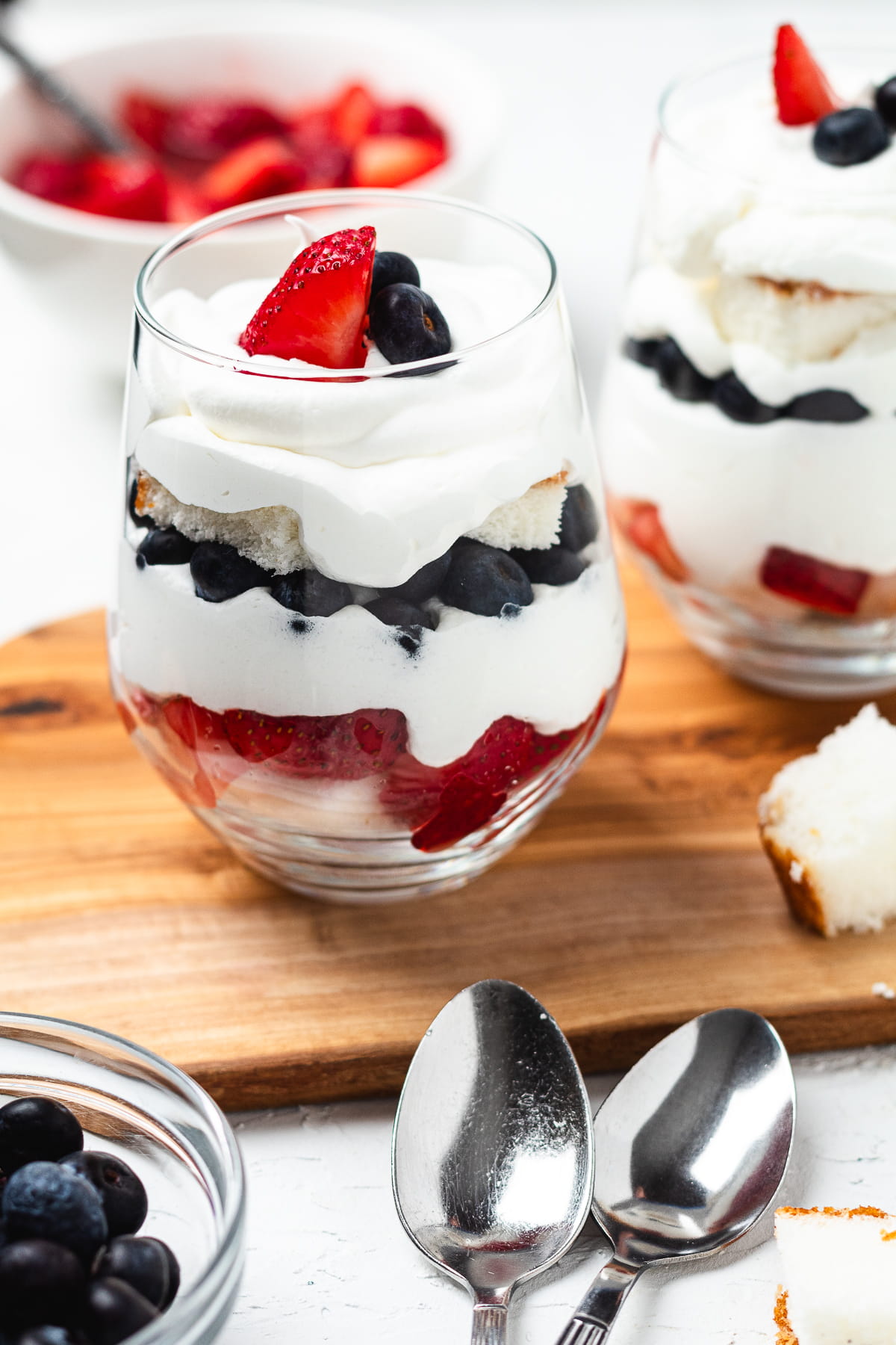 Trifles in glasses with layers of blueberries, strawberries, angel food cake, and whipped cream.