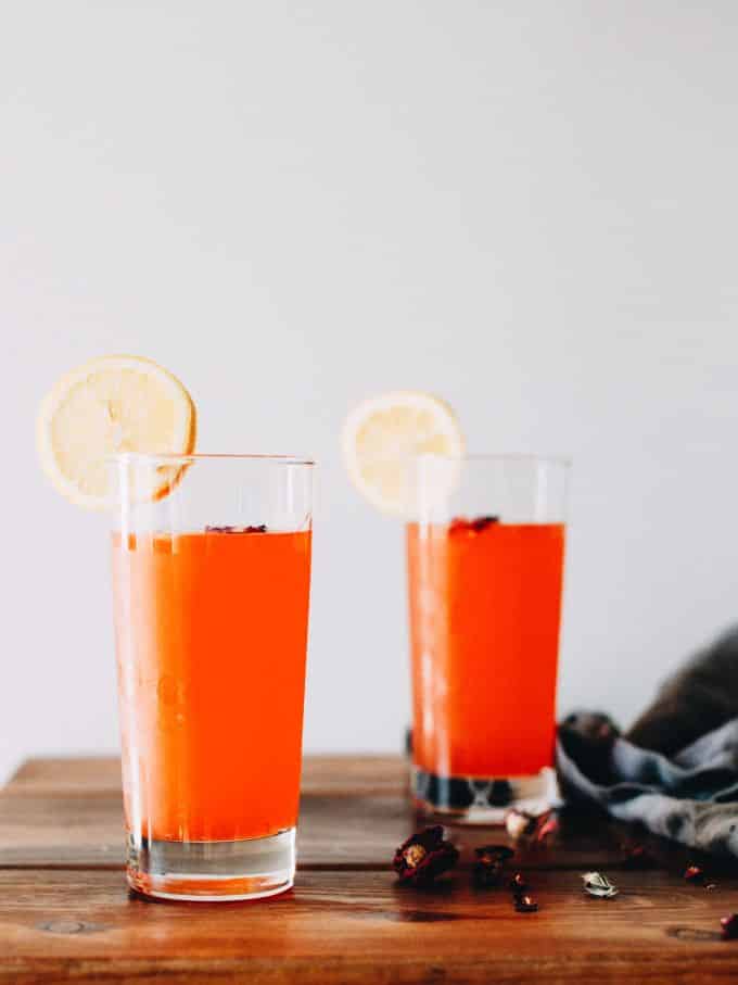 Glass of rose lemonade with lemon slices and ice against a light wall.