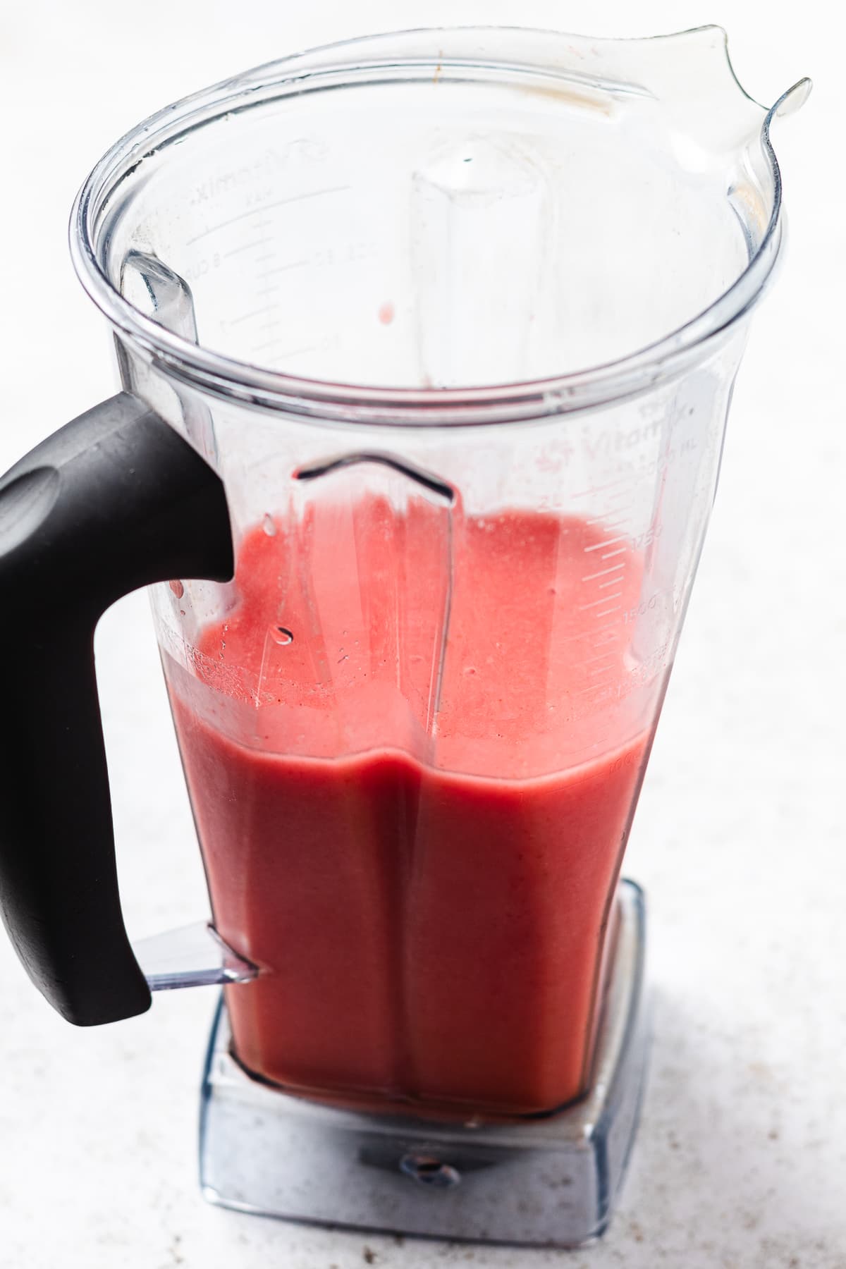 Blender container filled with thick pink red blended liquid on a light surface.