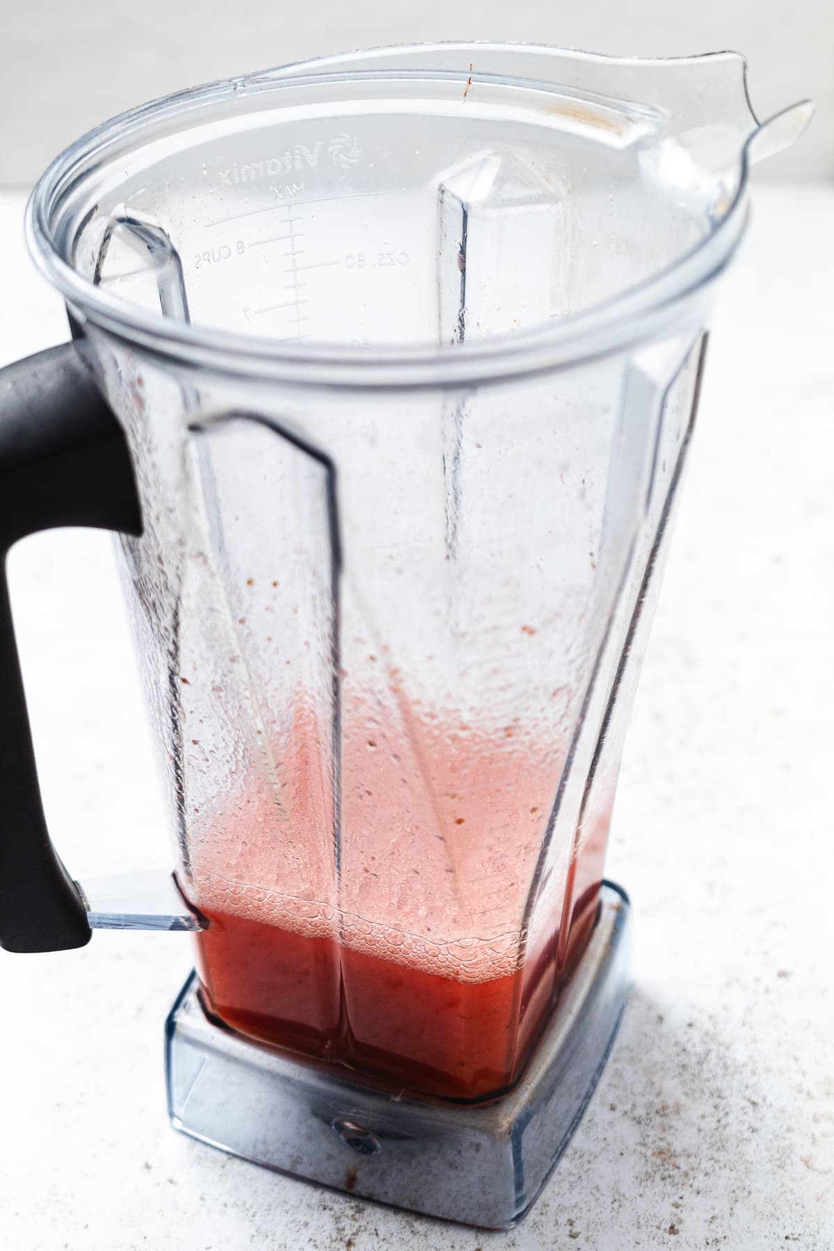 Pink red liquid being poured from a blender through a strainer into a metal cup.