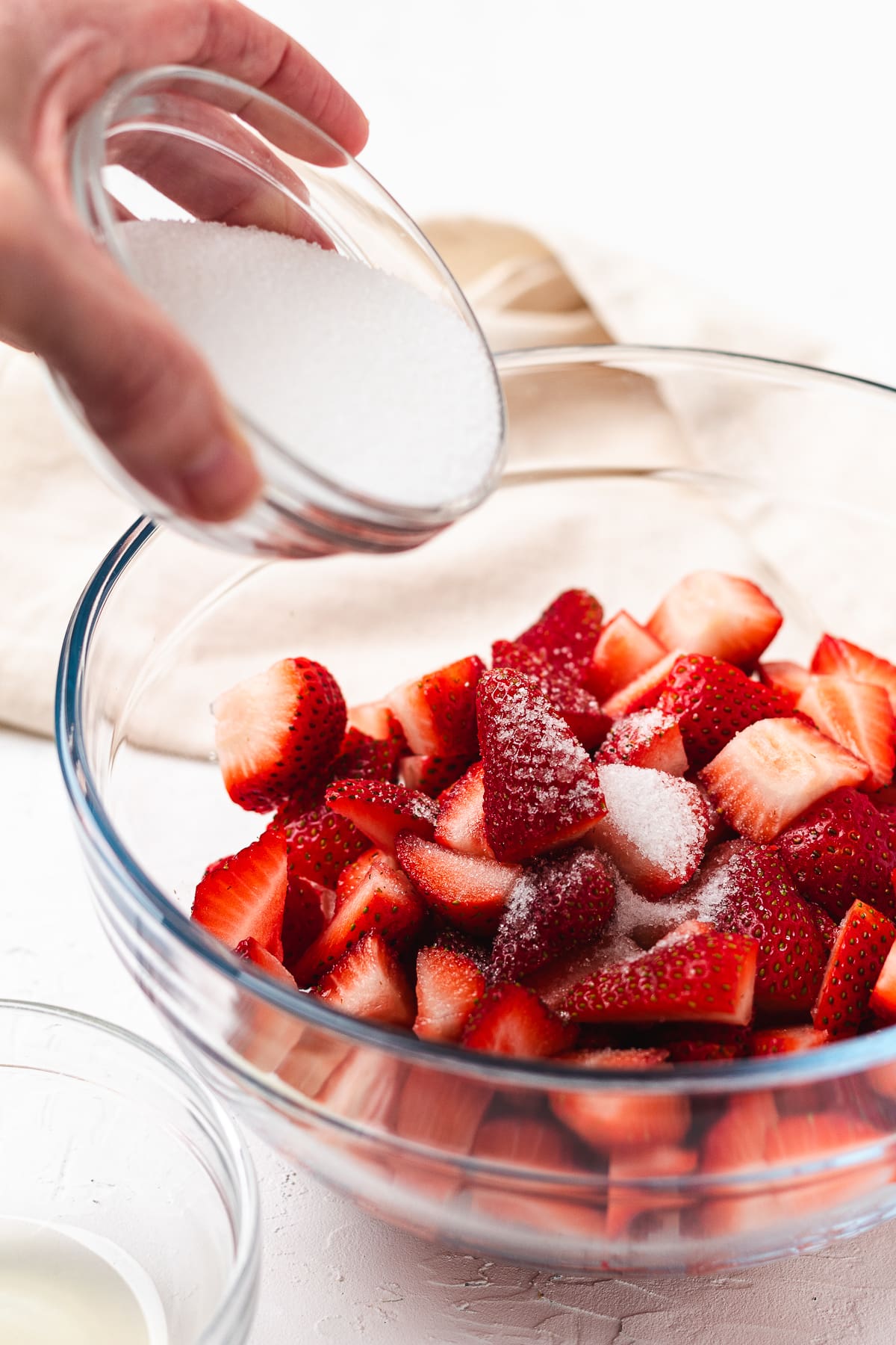 Adding sugar to fresh chopped strawberries in a glass bowl to make shortcake topping.
