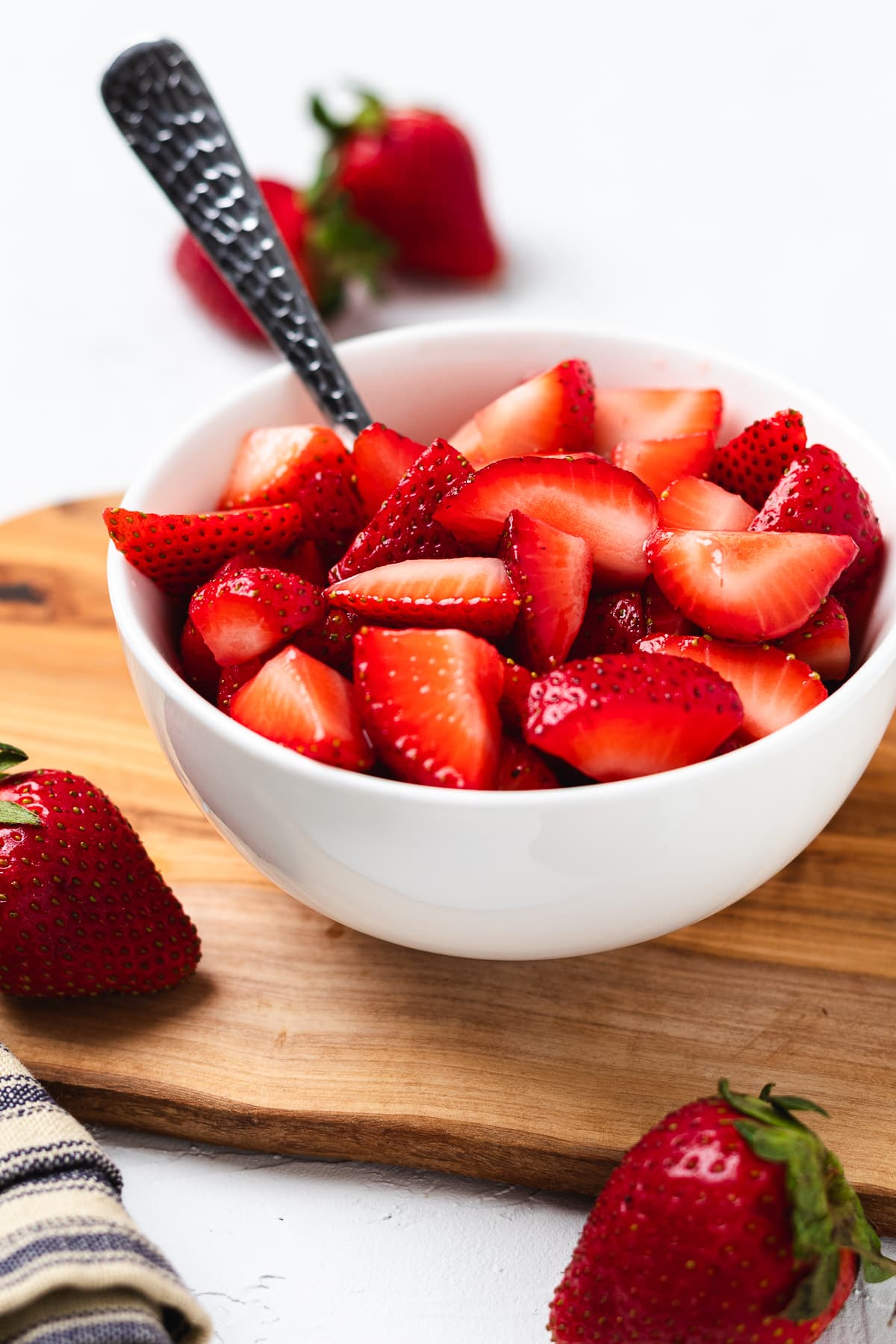 Bowl of fresh sliced strawberries with a spoon on a wooden board for shortcake topping.