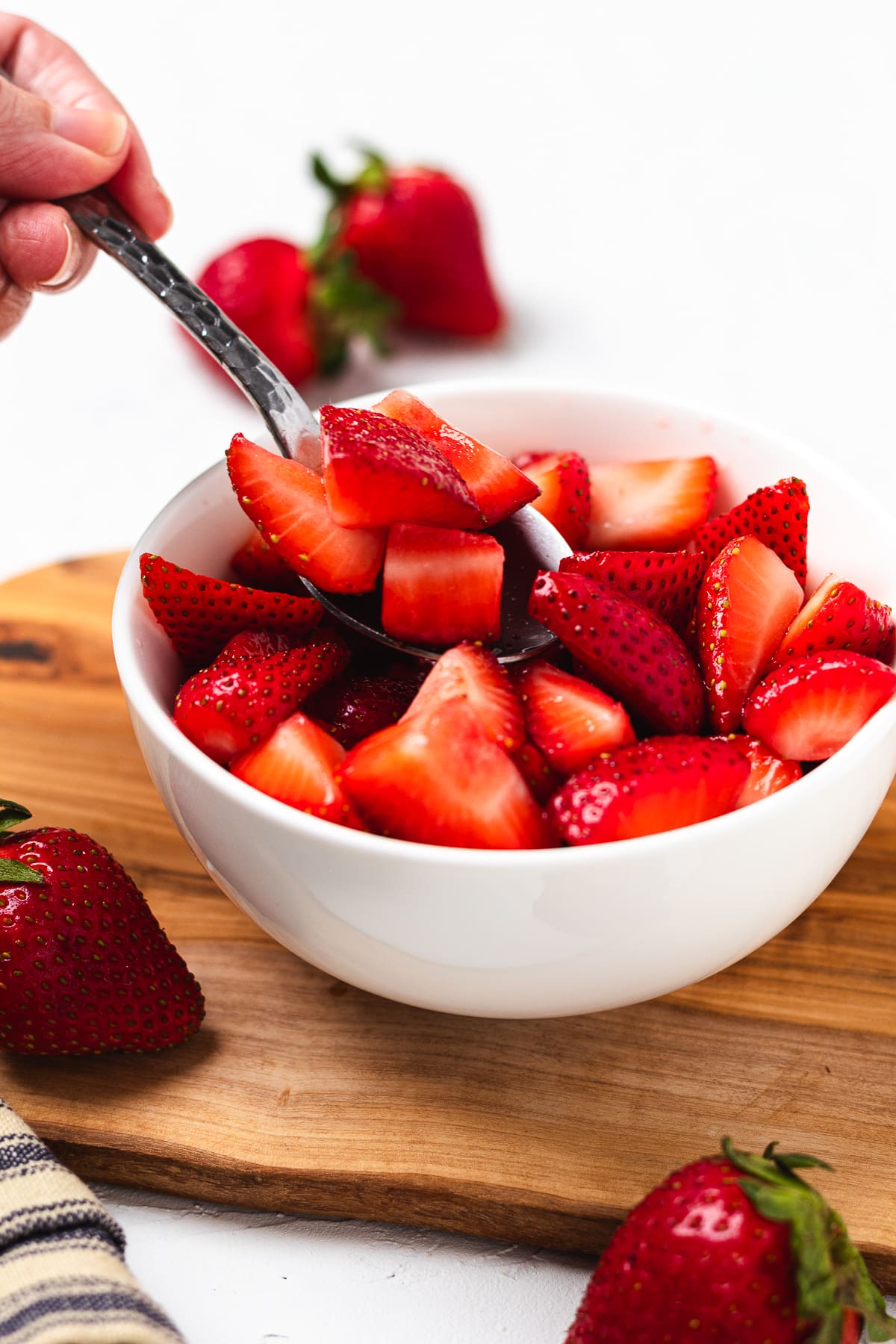 Spoon lifting juicy sliced strawberries from a bowl showing fresh shortcake topping.