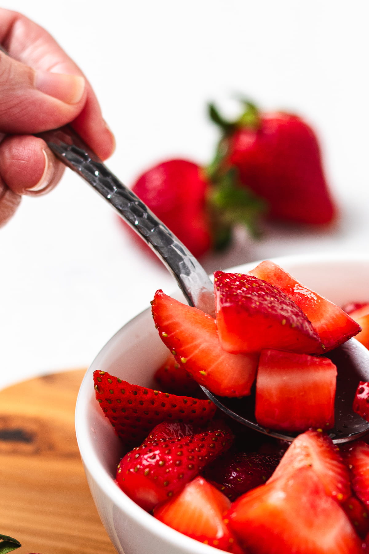 Close-up of spoon scooping fresh strawberries from a bowl with vibrant red color.