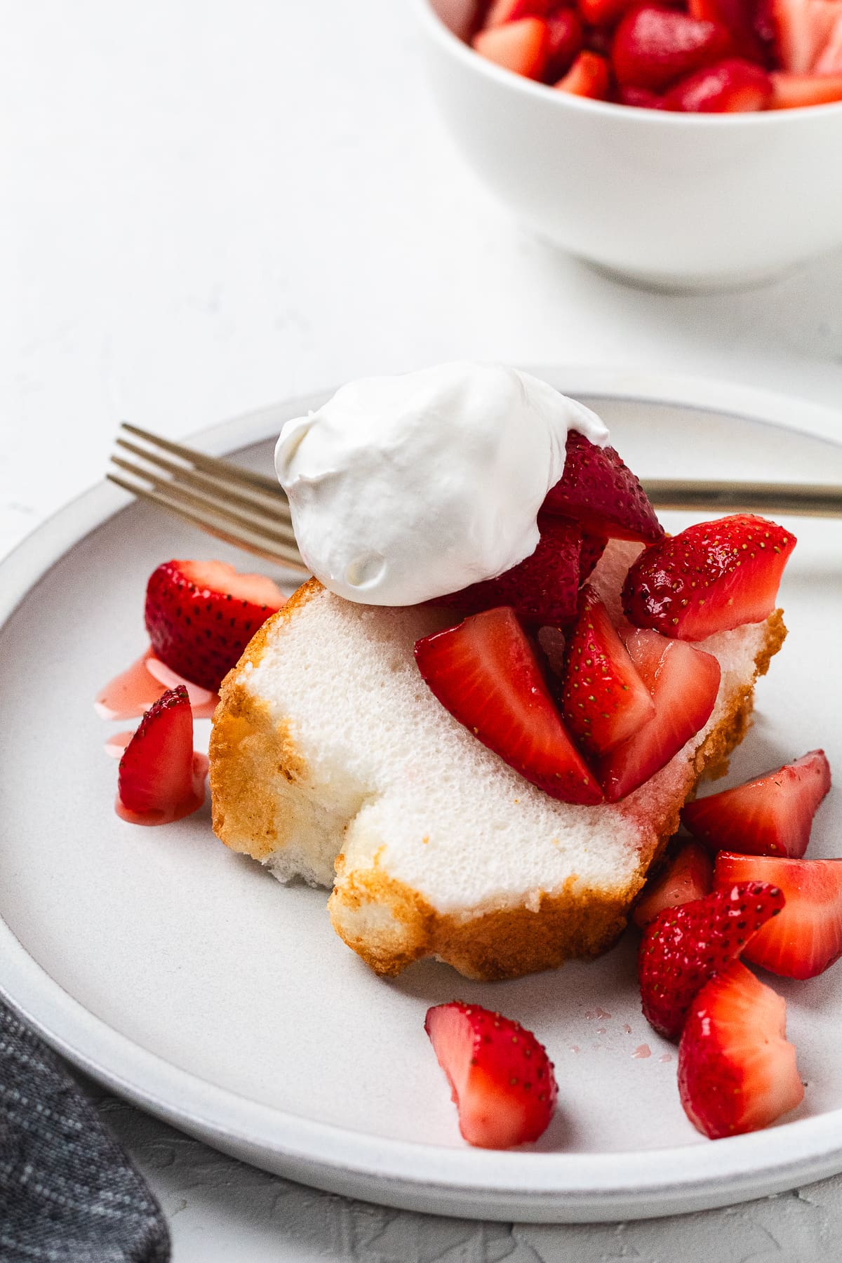 Angel food cake topped with whipped cream and fresh strawberries on a plate with syrup drizzle.
