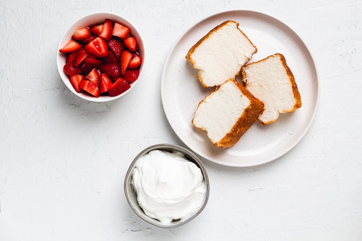 Ingredients for strawberry shortcake with angel food cake including berries, cake slices, and whipped cream.