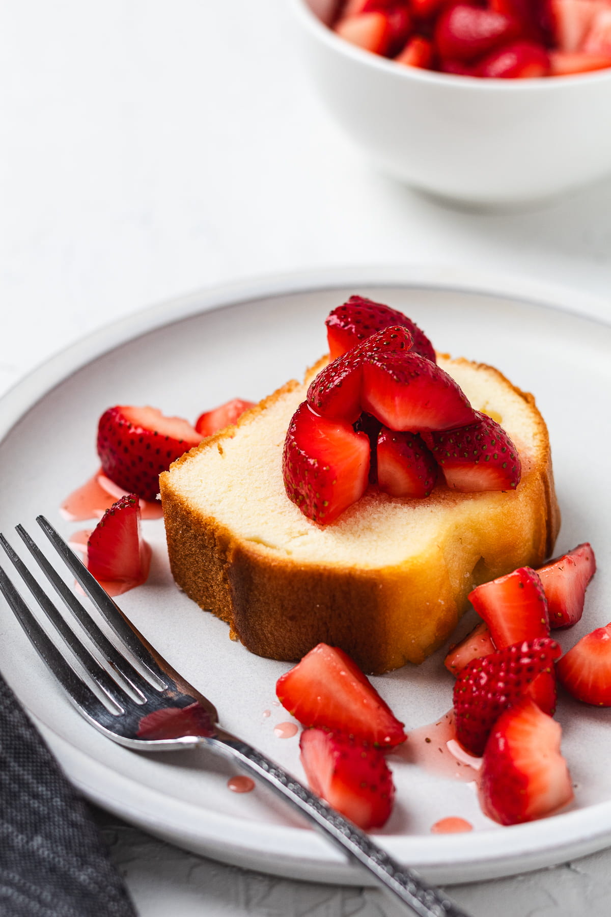 Pound cake slice topped with fresh strawberries on a plate with scattered berries and syrup.