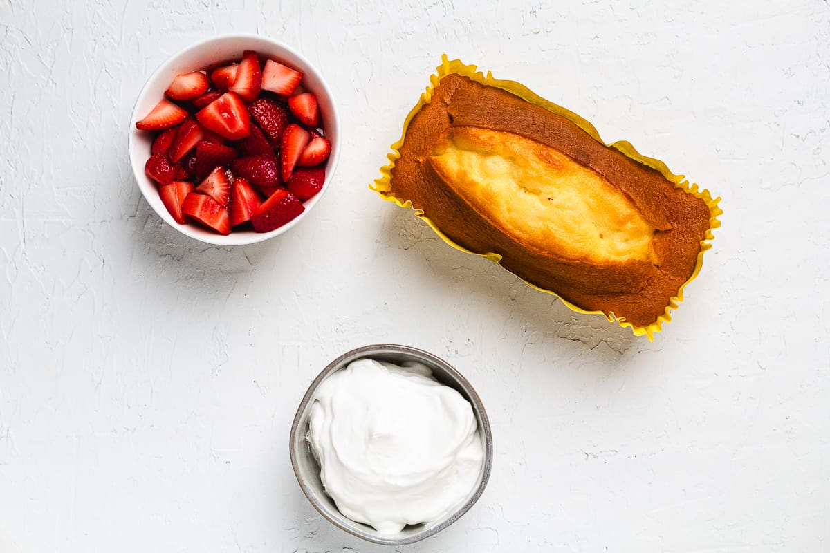 Ingredients for strawberry shortcake with pound cake including sliced berries, cake, and whipped cream.