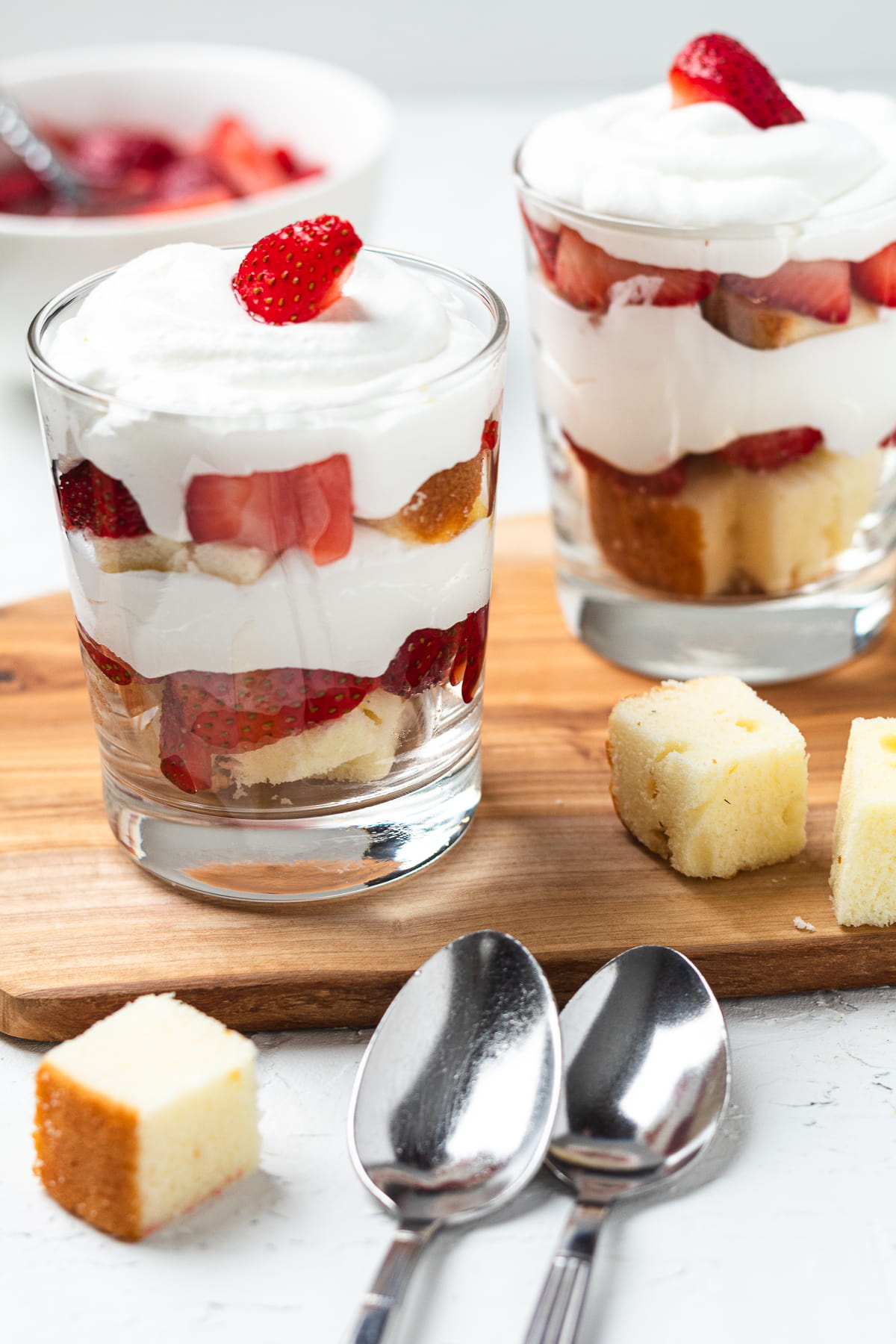 Trifles layered with chopped strawberries, pound cake, and whipped cream in glasses.