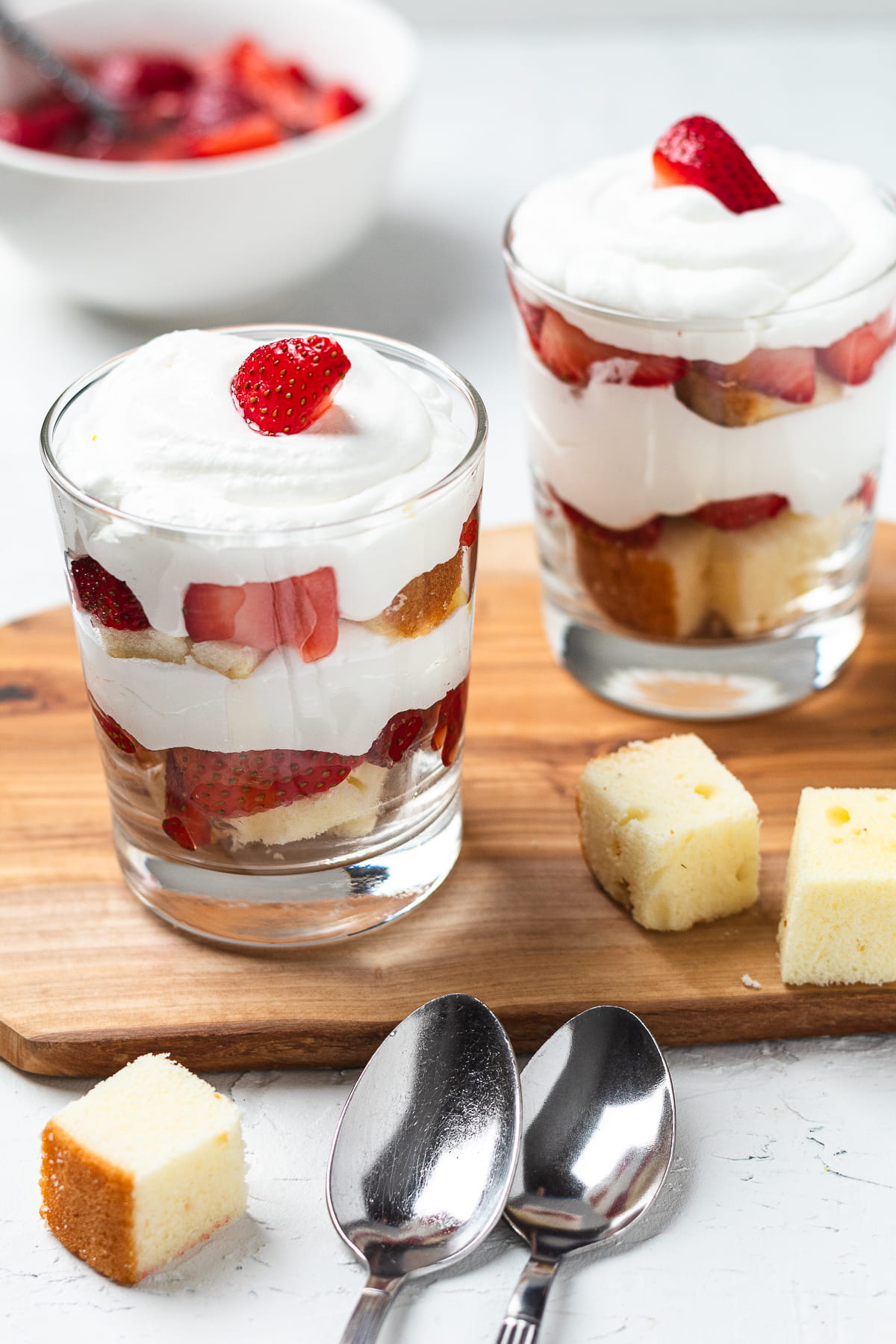 Strawberry trifle cups with cake cubes, whipped cream, and fresh berries served in small glasses.