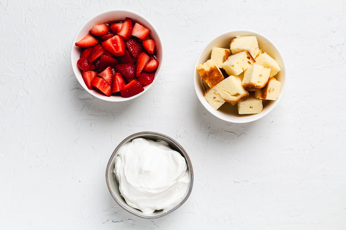 Ingredients for strawberry trifle cups including sliced strawberries, cake cubes, and whipped cream.