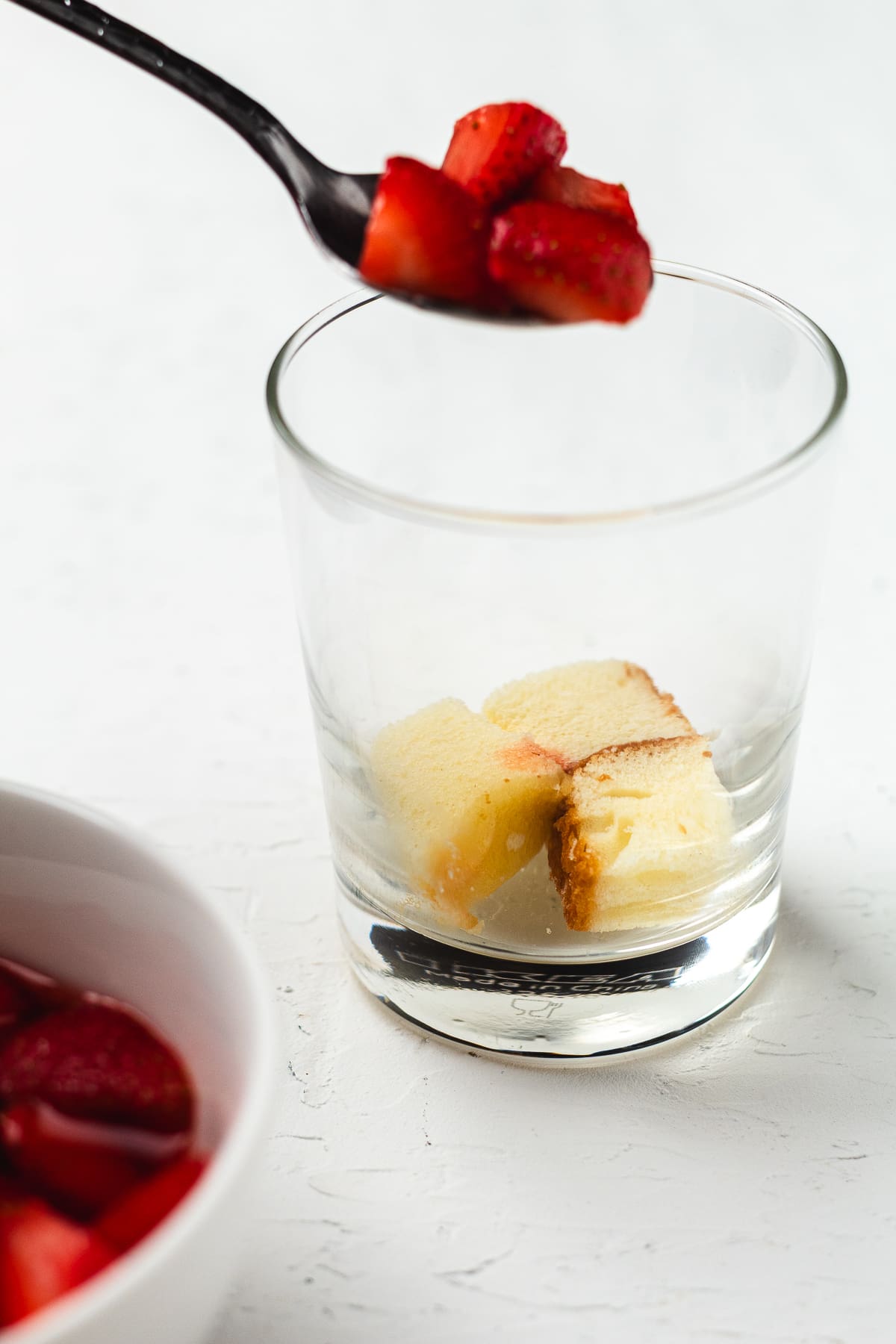 Adding fresh strawberries to a glass with cake cubes to build mini strawberry trifle dessert cups.