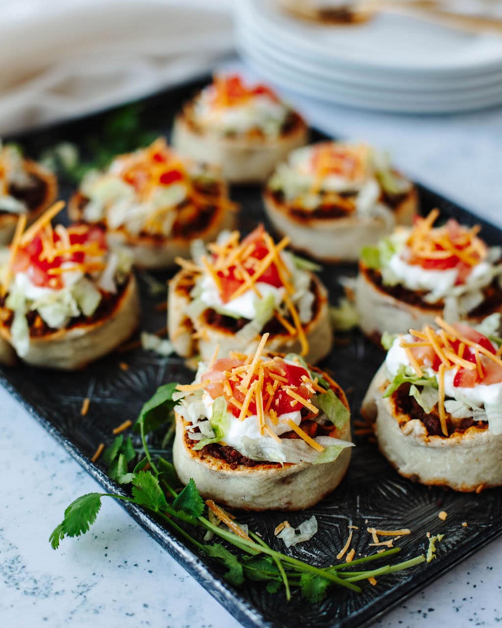 Taco pinwheels topped with lettuce, tomatoes, cheese, and sour cream on a platter.