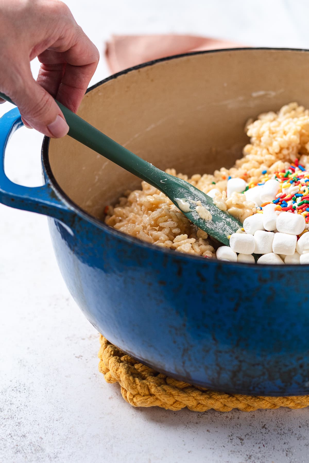Hand stirring birthday cake Rice Krispie treat mixture with marshmallows and sprinkles.