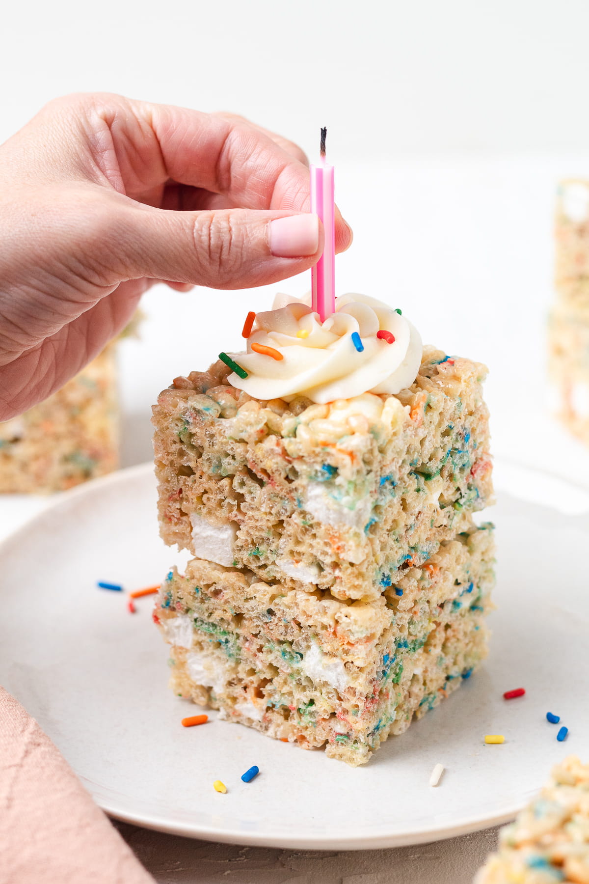Hand placing candle into Birthday Cake Rice Krispie treats topped with frosting.