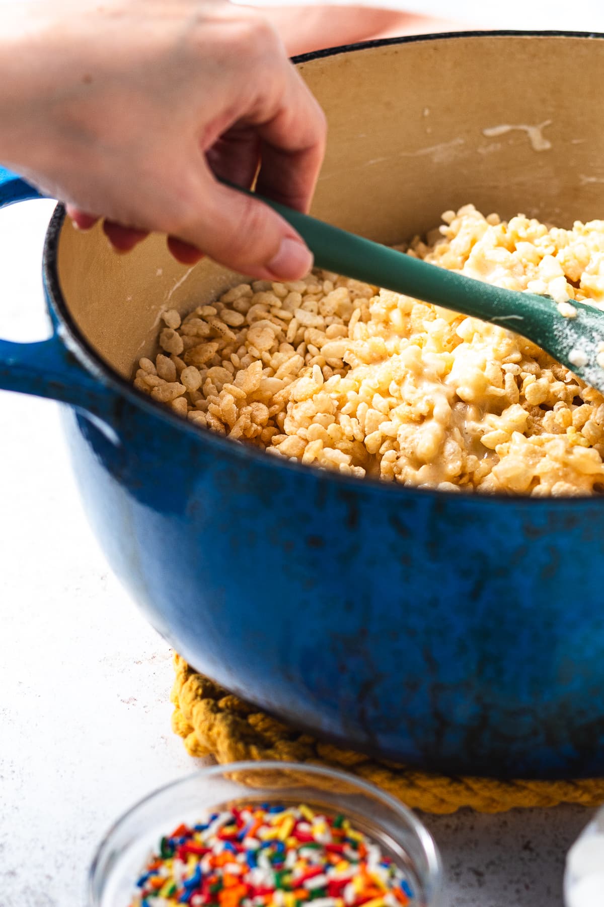 Mixing Rice Krispies cereal into marshmallow mixture in a blue pot.