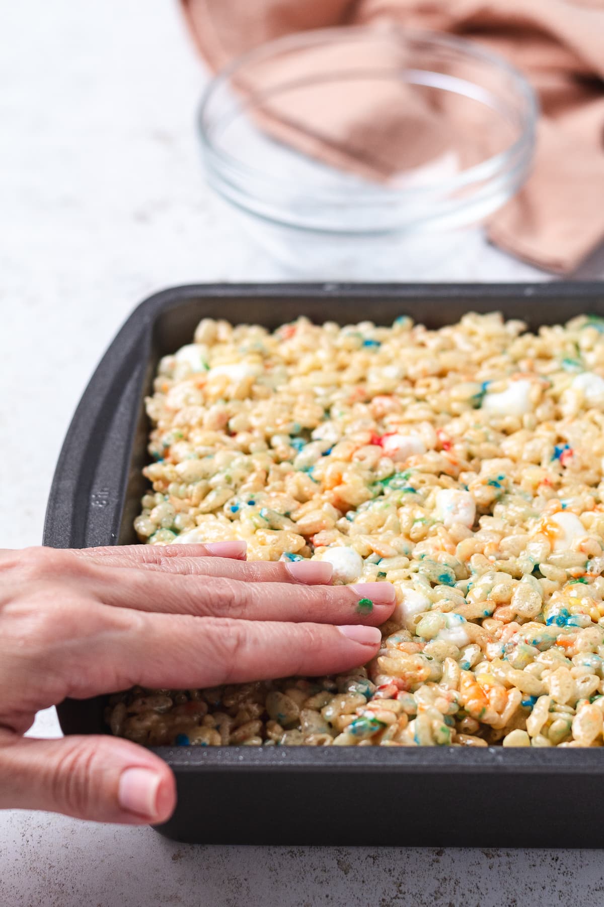 Pressing Birthday Cake Rice Krispie treat mixture into a baking pan.