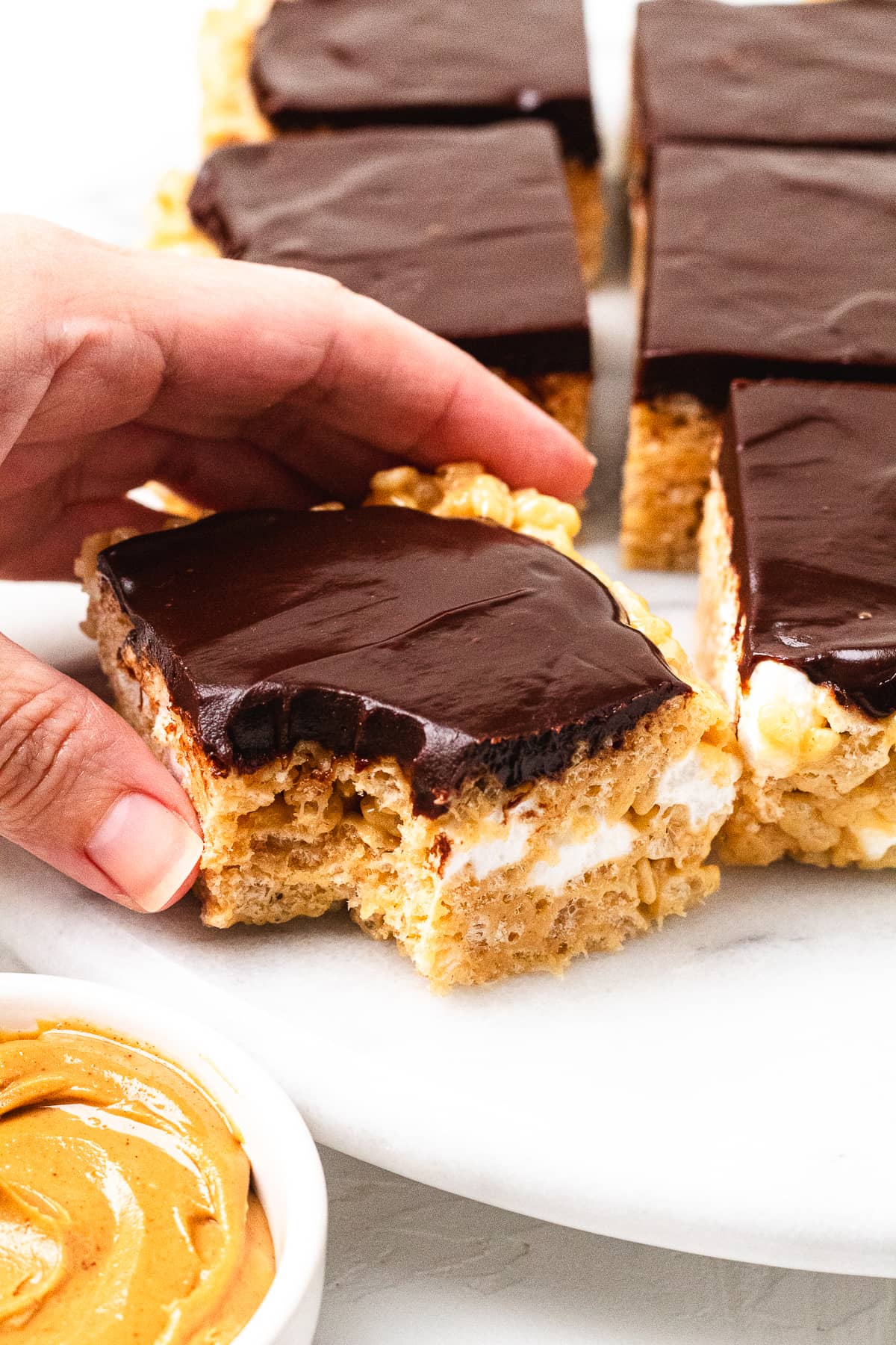 Hand holding a bitten chocolate peanut butter Rice Krispie treat with chocolate topping.