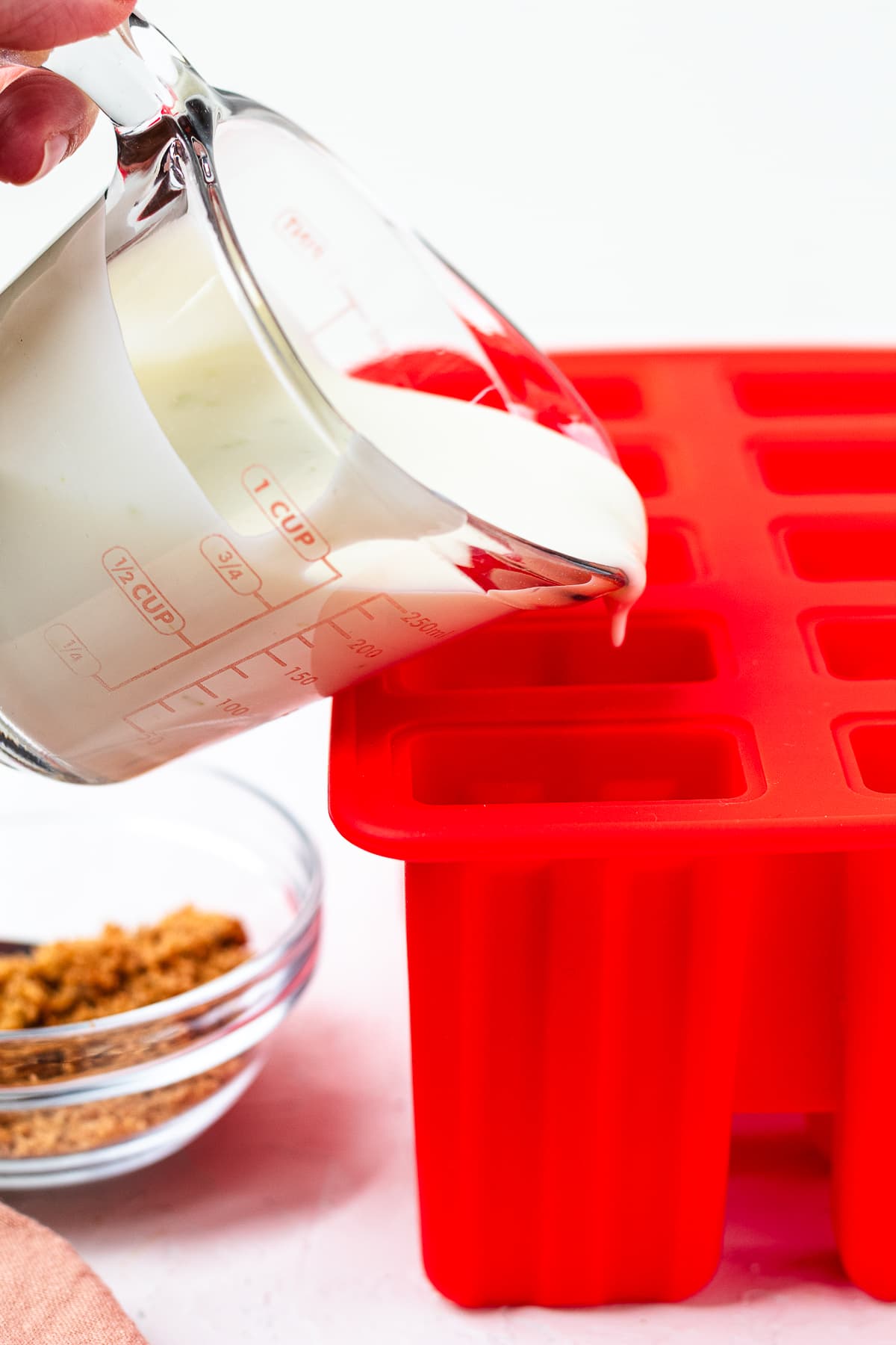 Pouring key lime pie popsicle mixture into molds.