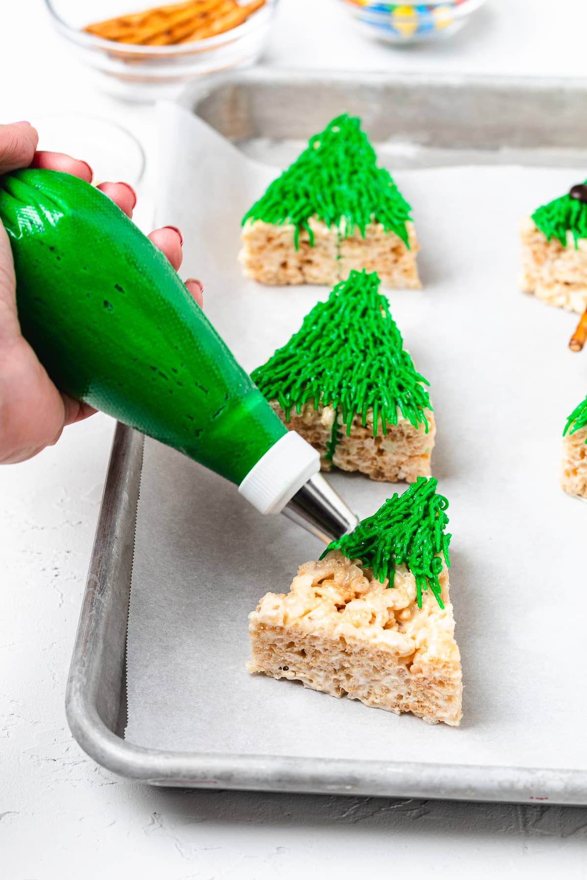 Piping green frosting onto Christmas tree Rice Krispie treat.