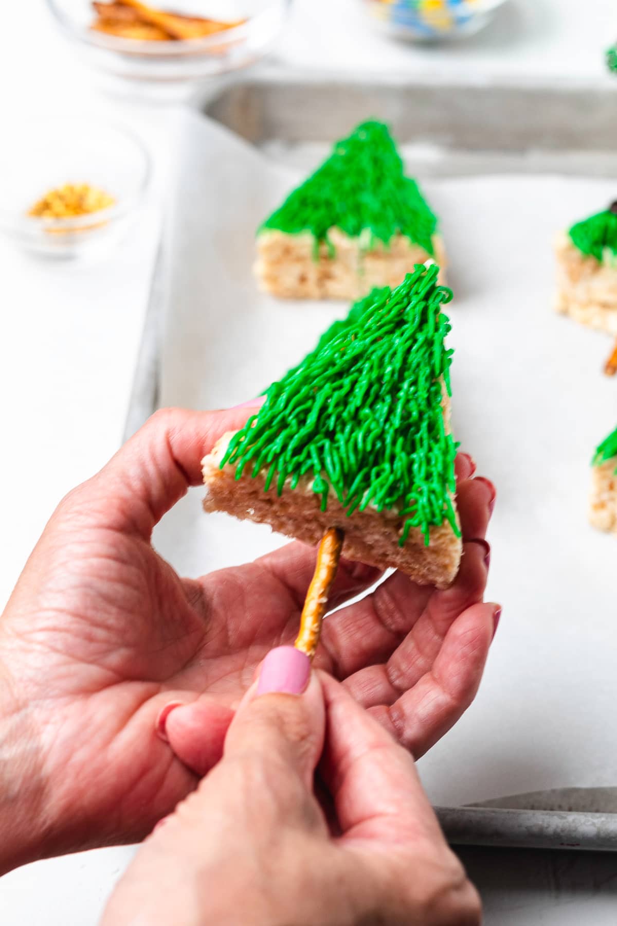 Inserting pretzel stick into Christmas tree Rice Krispie treat.