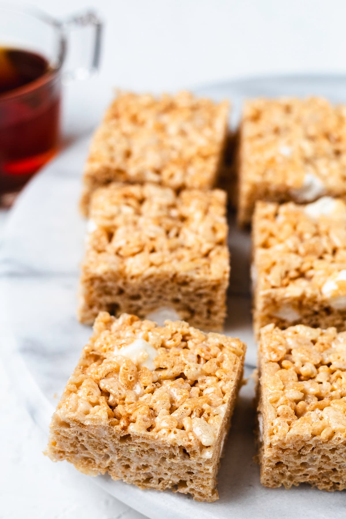 Close-up of thick apple cider Rice Krispie treats on a serving board with apple cider in the background.