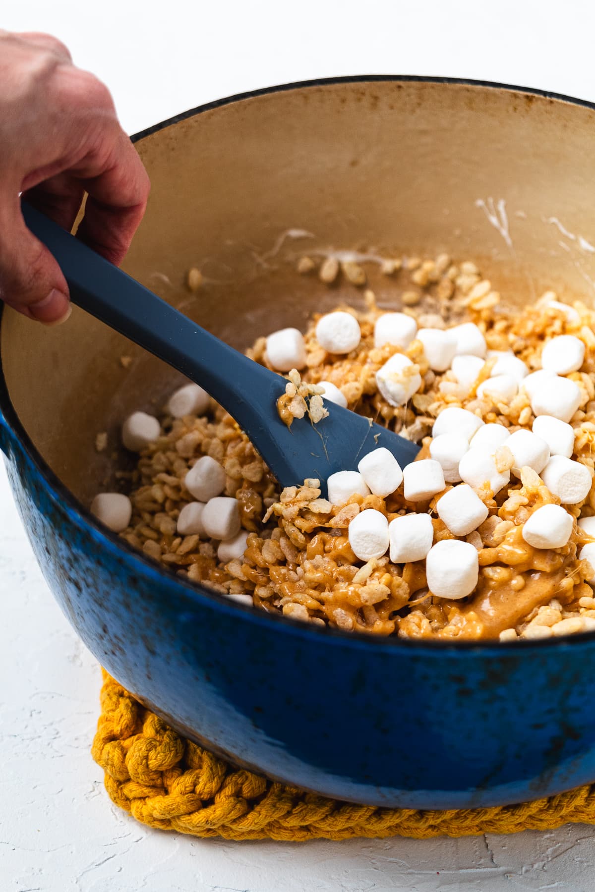Mini marshmallows added to warm peanut butter Rice Krispie treat mixture in a Dutch oven.