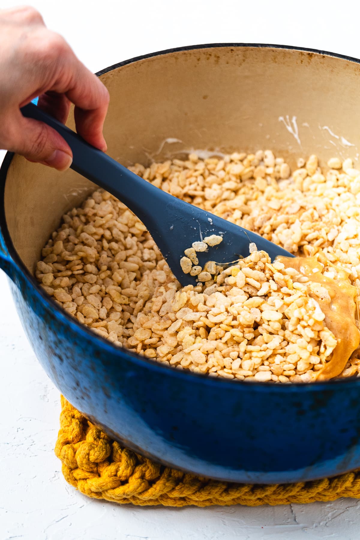 Rice Krispies being folded into melted peanut butter marshmallow mixture with a silicone spatula.