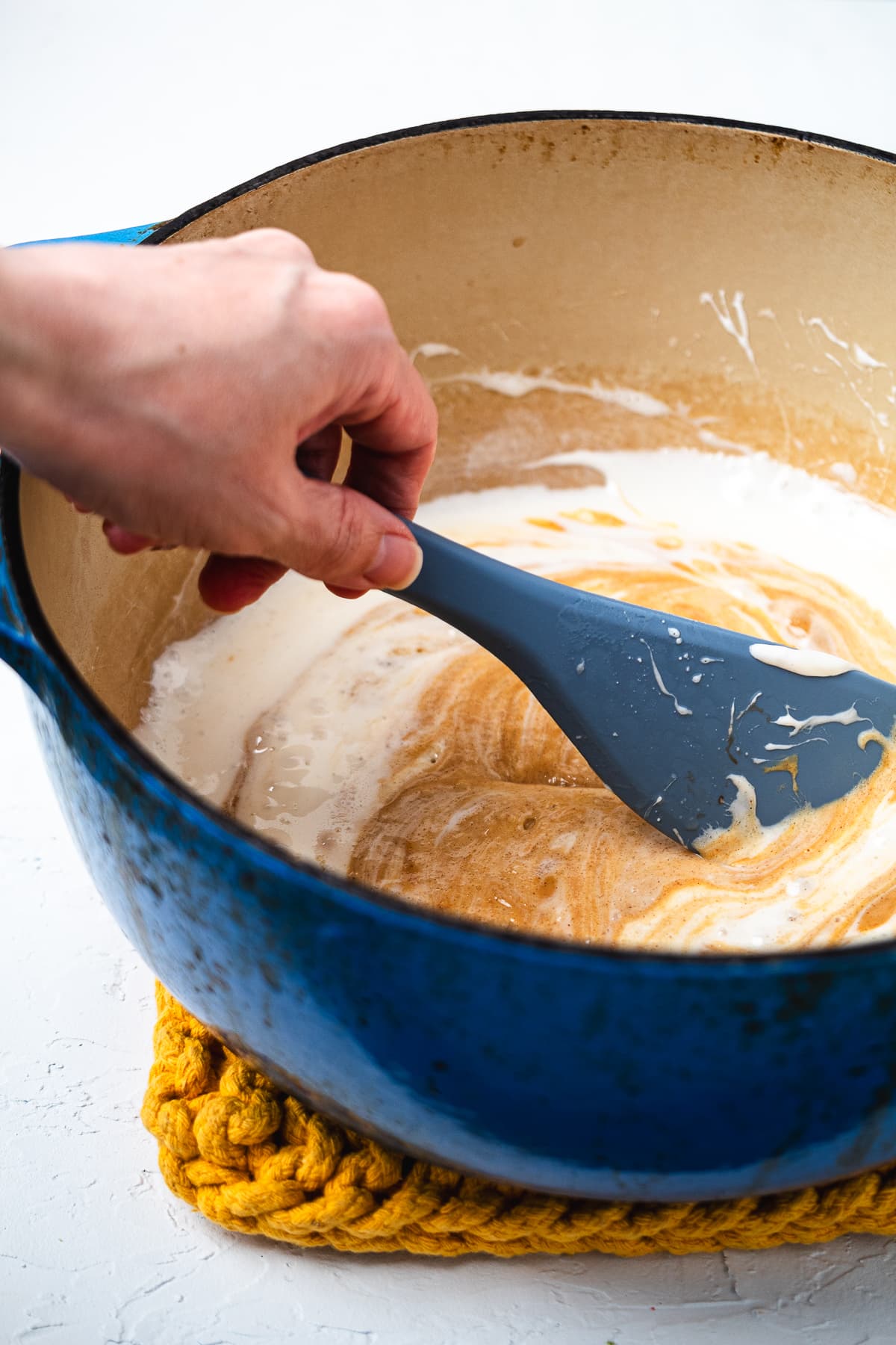 Hand stirring melted marshmallow and peanut butter mixture in a blue Dutch oven with a silicone spatula.