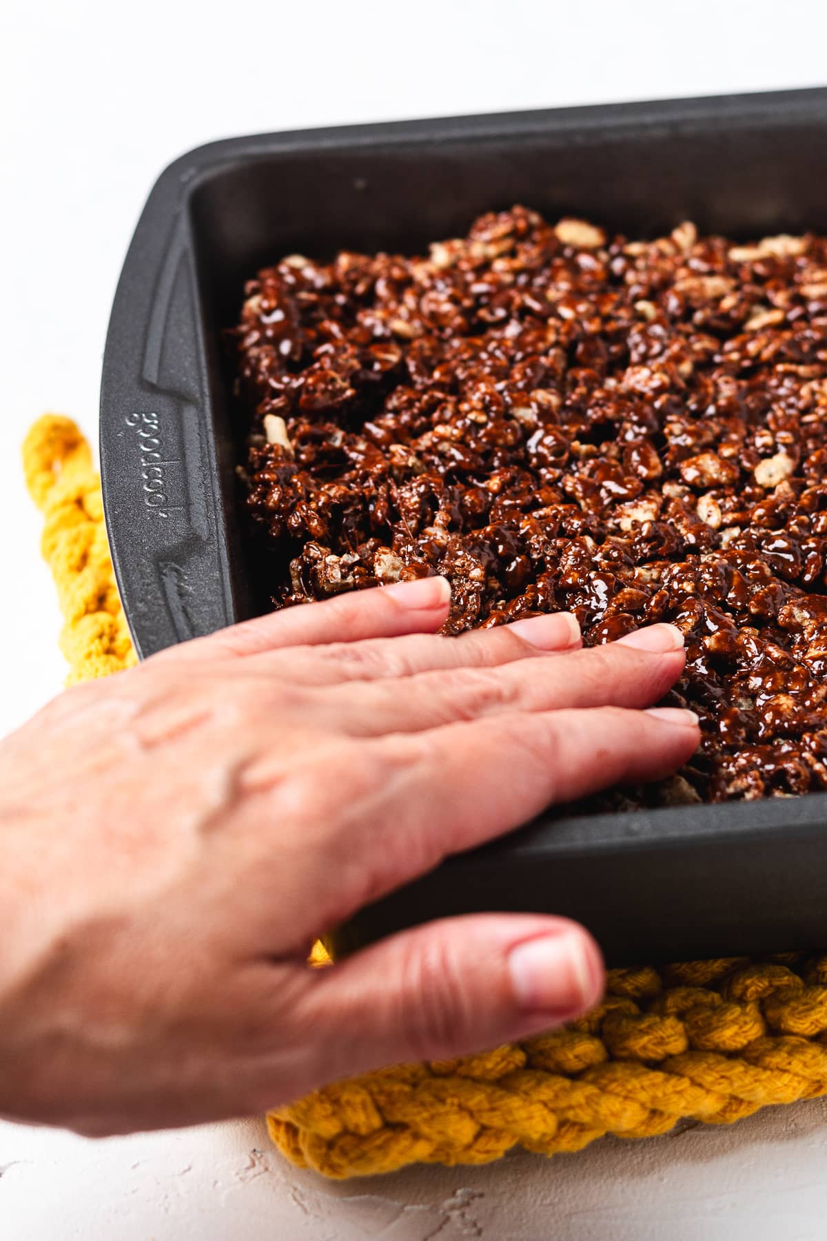Pressing chocolate Rice Krispie treats into a pan.