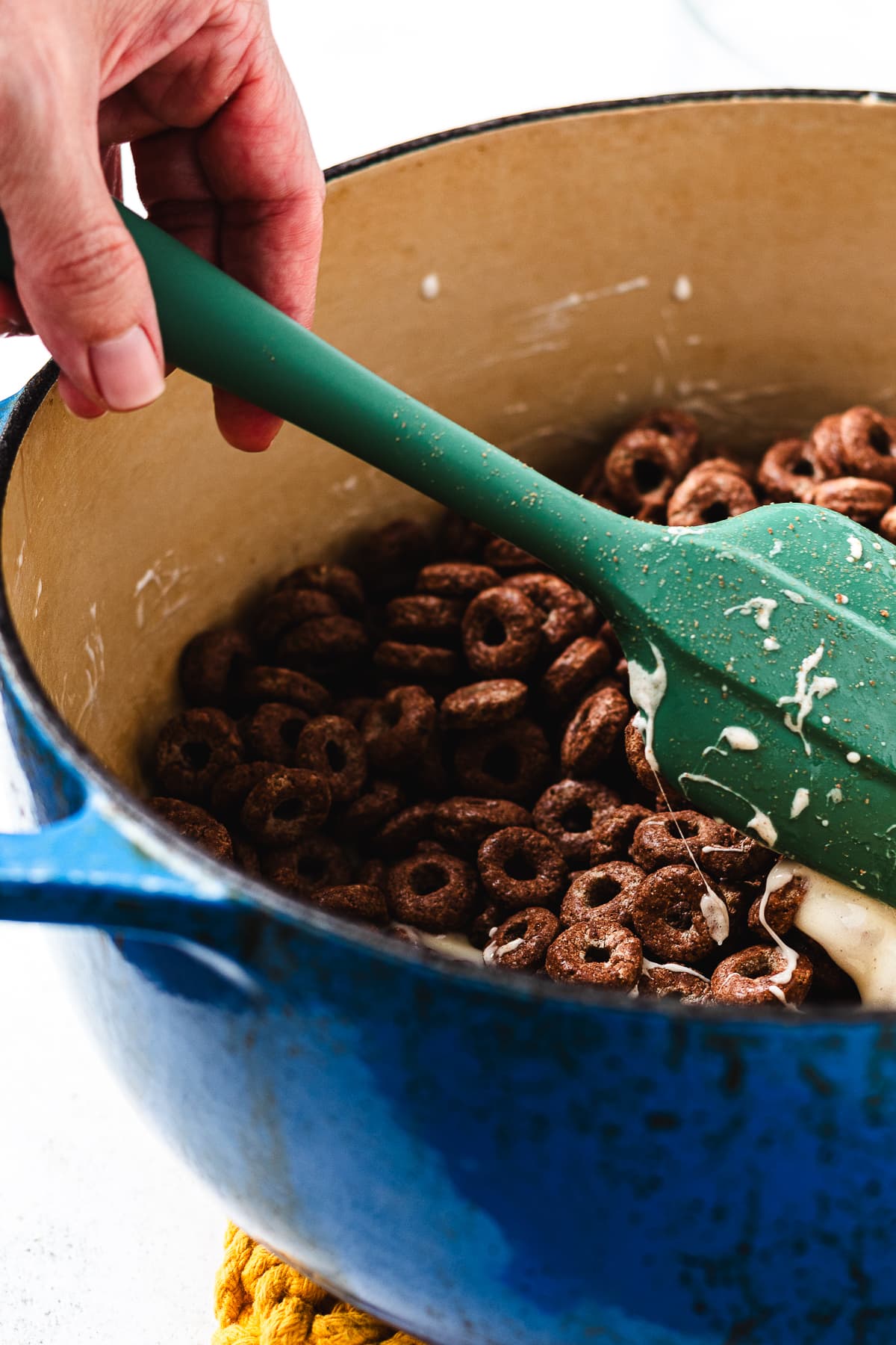 Hand folding Cocoa Loops cereal into melted marshmallow mixture