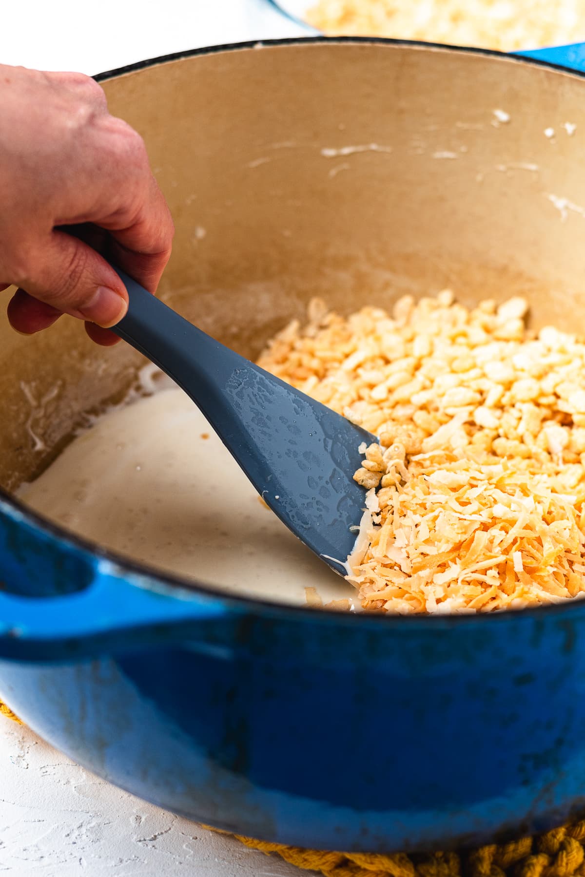 Rice Krispies cereal and toasted coconut being folded into melted marshmallows.