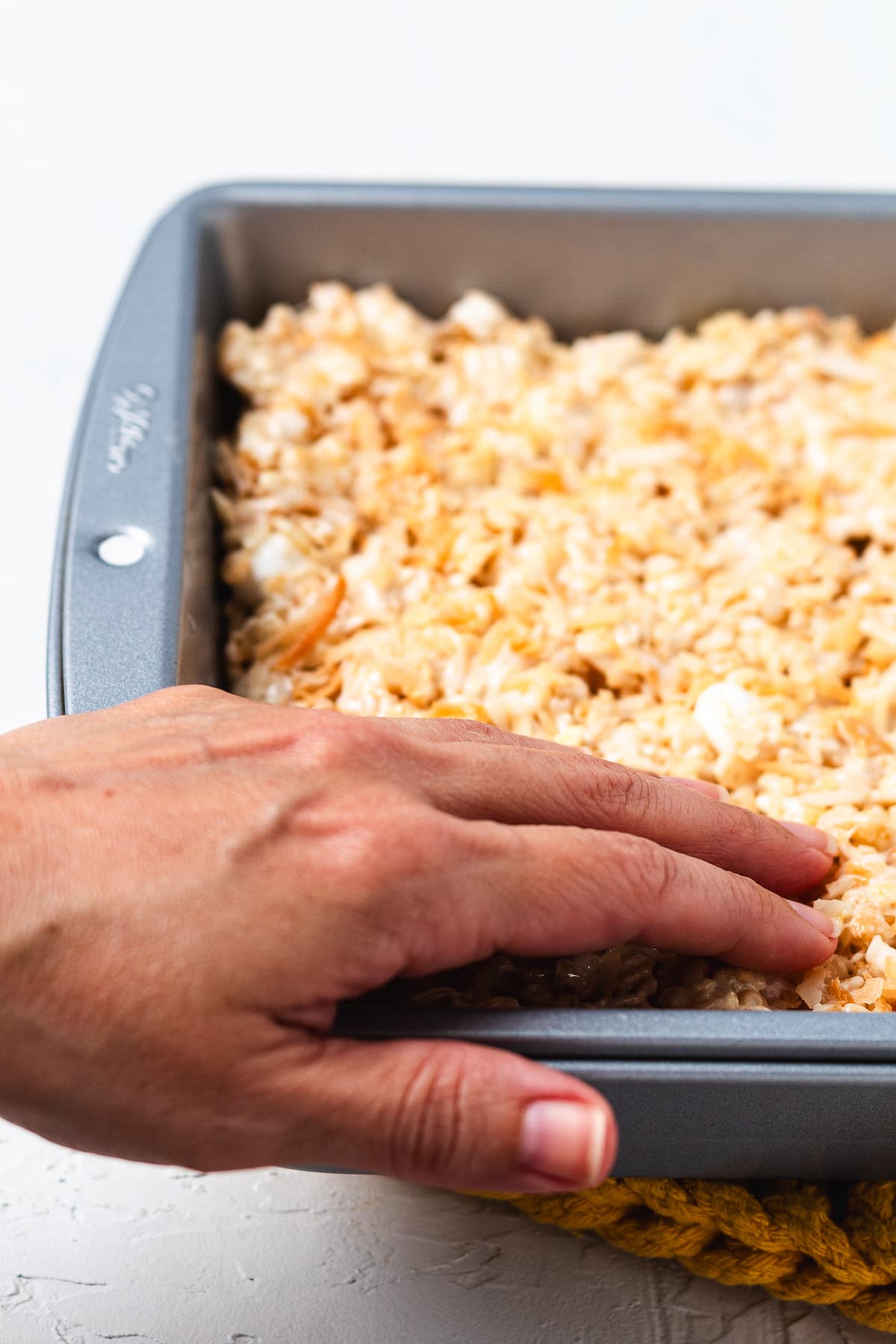 Hand pressing coconut Rice Krispie treat mixture into a baking pan.