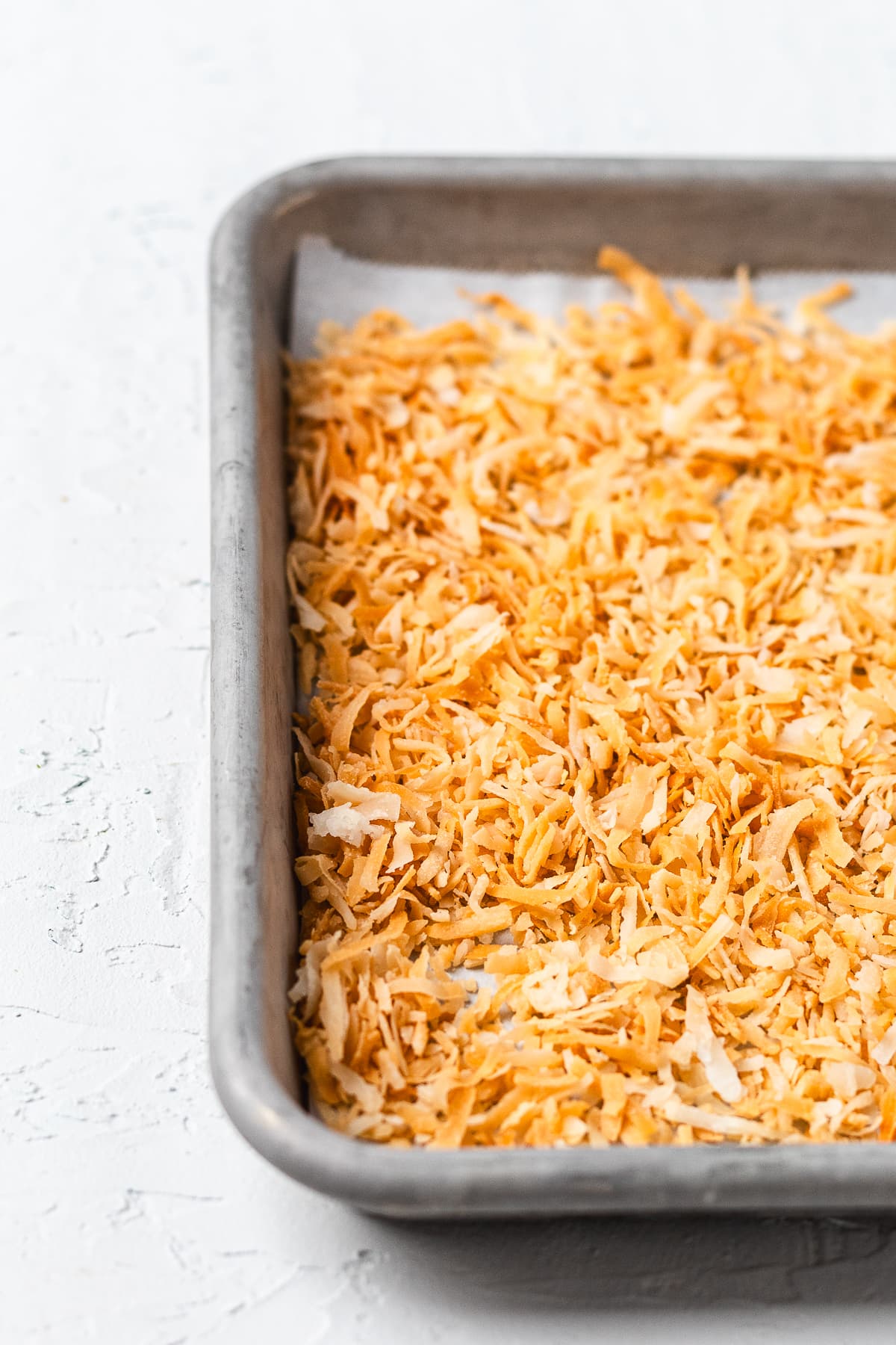 Toasted coconut spread evenly on top of Rice Krispie treats in a baking pan.