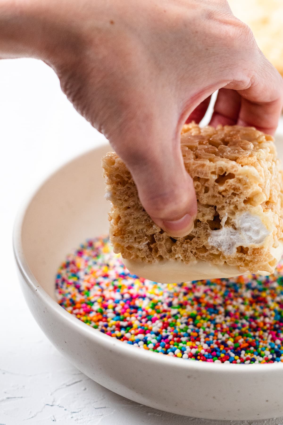 Dipping a frosted Rice Krispie treat into rainbow dot sprinkles.