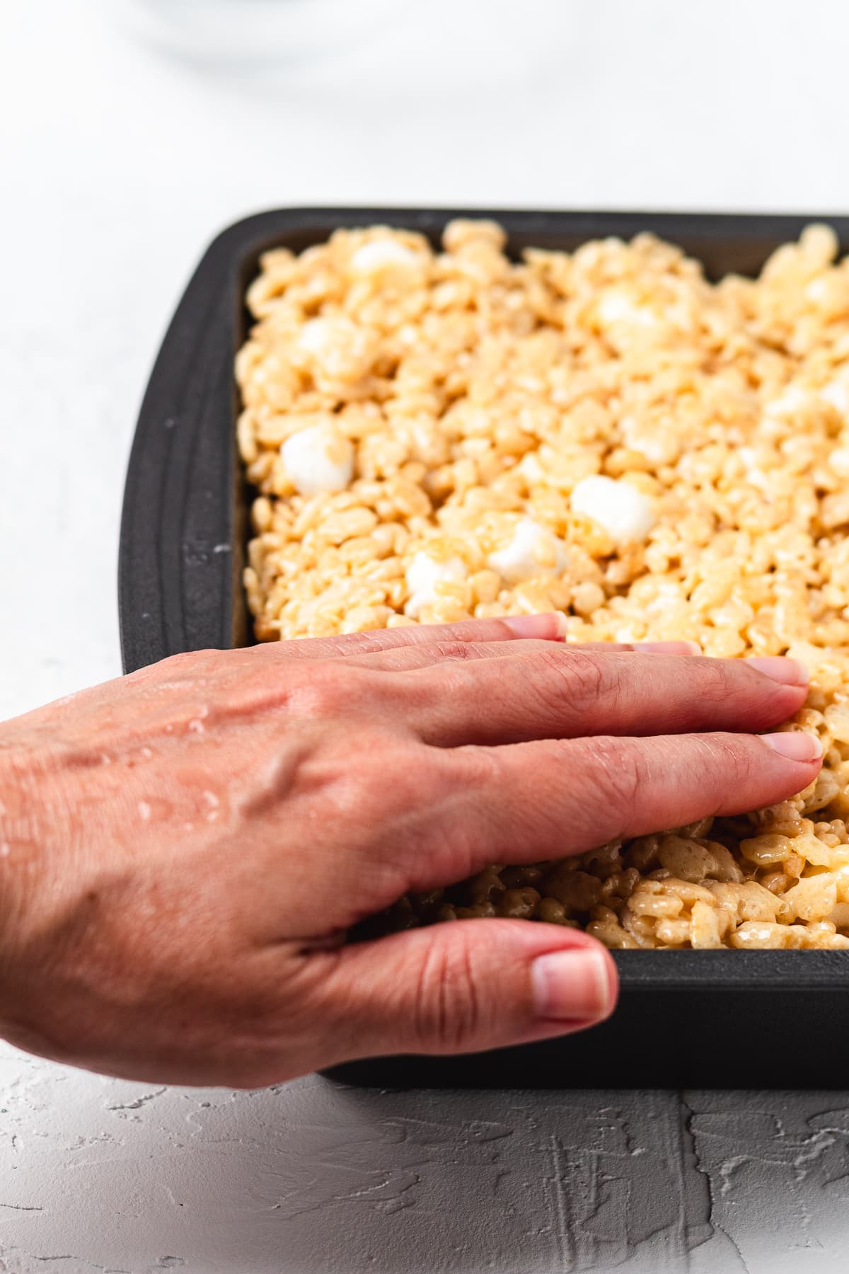Pressing the Rice Krispie treat mixture into a 9x13 pan.