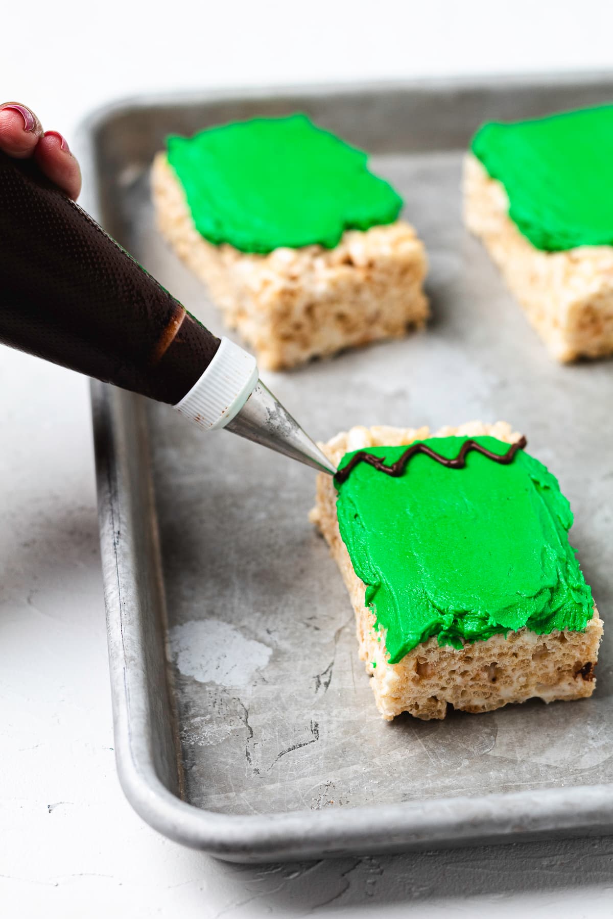 Piping chocolate frosting hair onto a Frankenstein Rice Krispie treat.