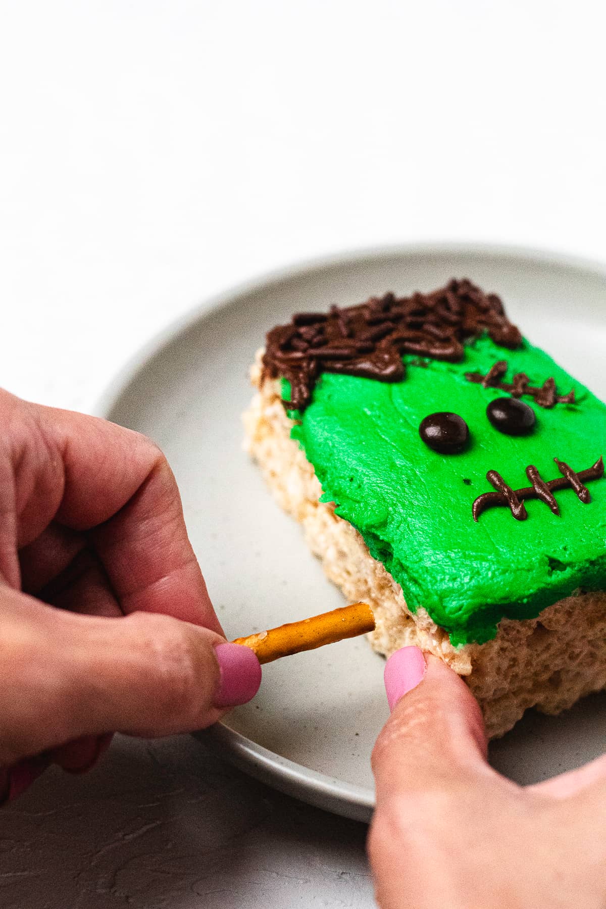 Hand inserting pretzel stick into Frankenstein Rice Krispie treat for monster bolts.