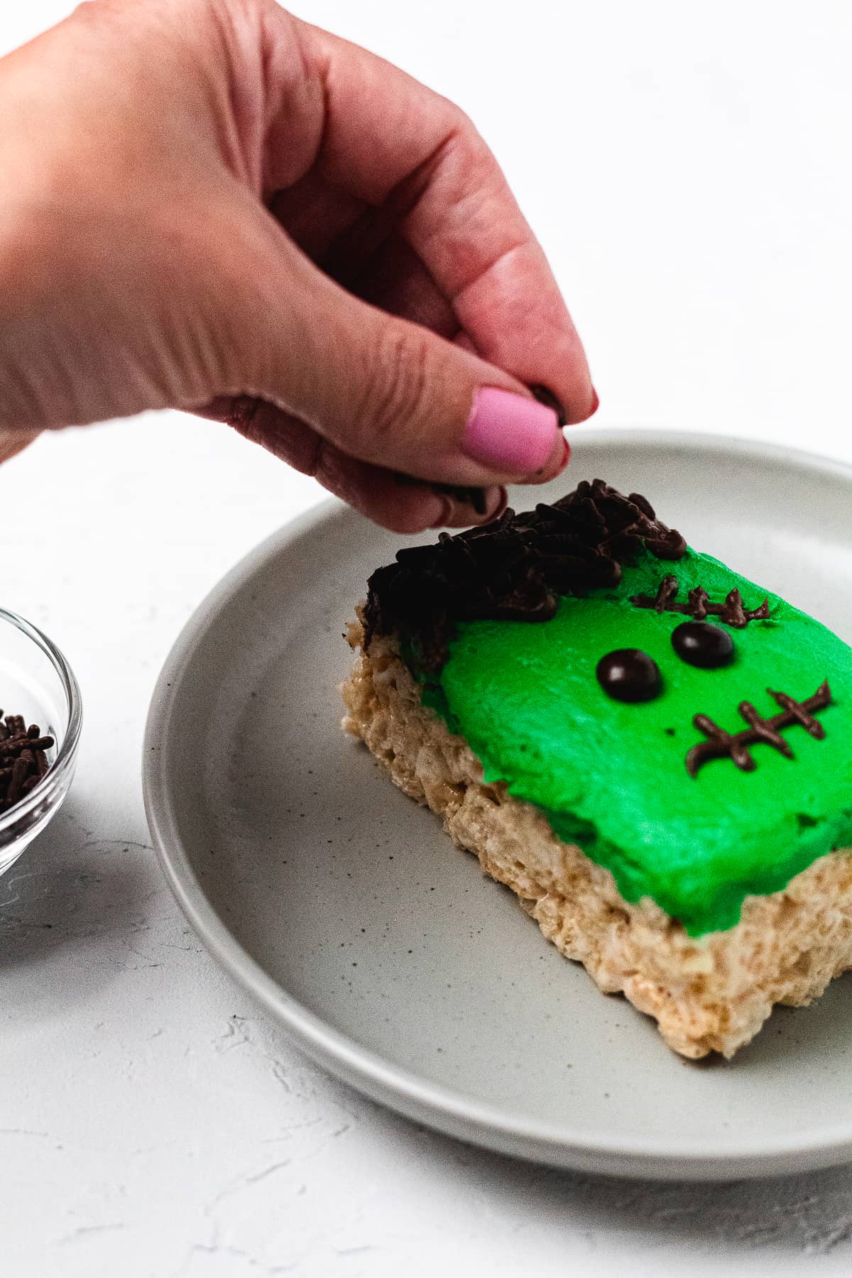 Adding chocolate sprinkles to frosting hair on Frankenstein Rice Krispie treat.