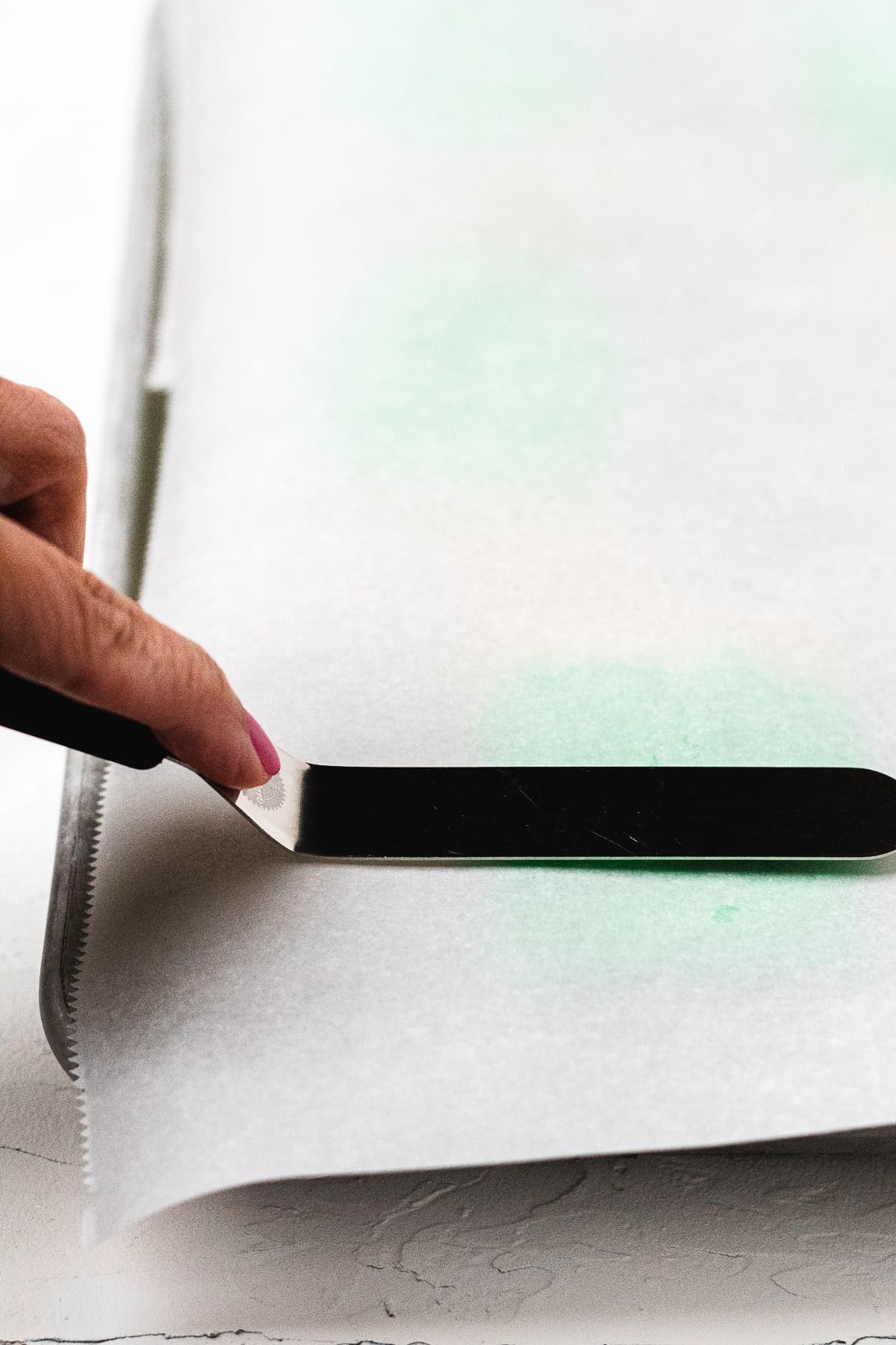 Offset spatula smoothing green frosting over Rice Krispie treat.