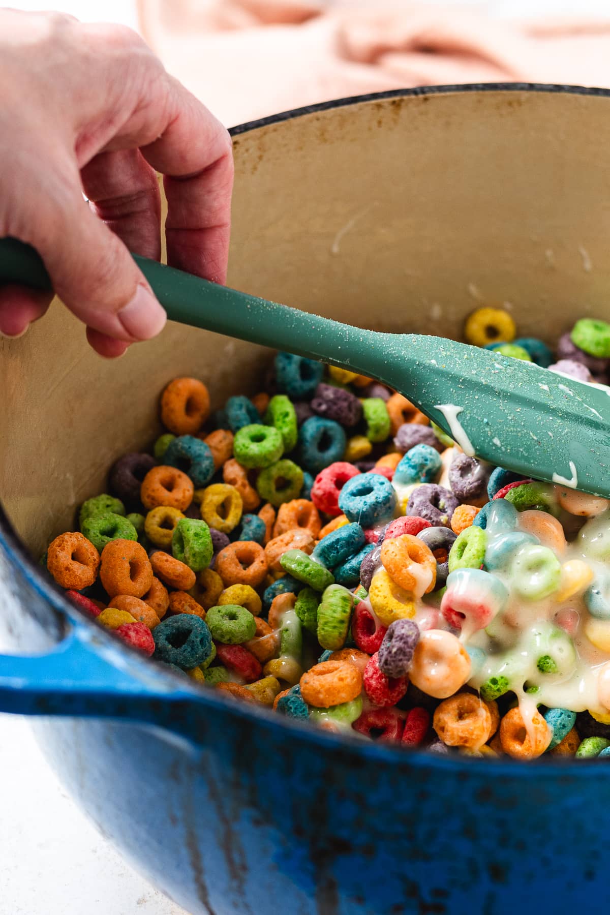 Mixing Froot Loops cereal into melted marshmallows.