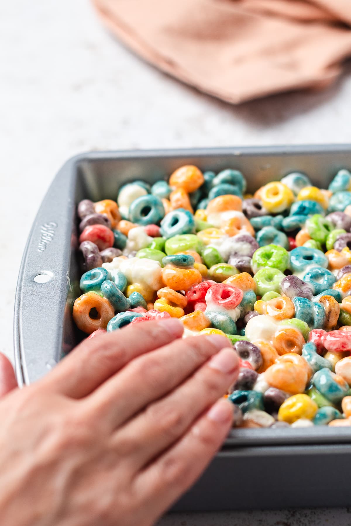 Pressing Froot Loops Rice Krispie Treats into a pan.