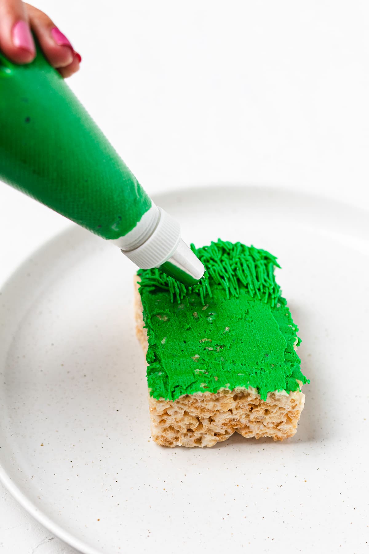 Piping green frosting onto a Grinch Rice Krispie treat with a grass tip.