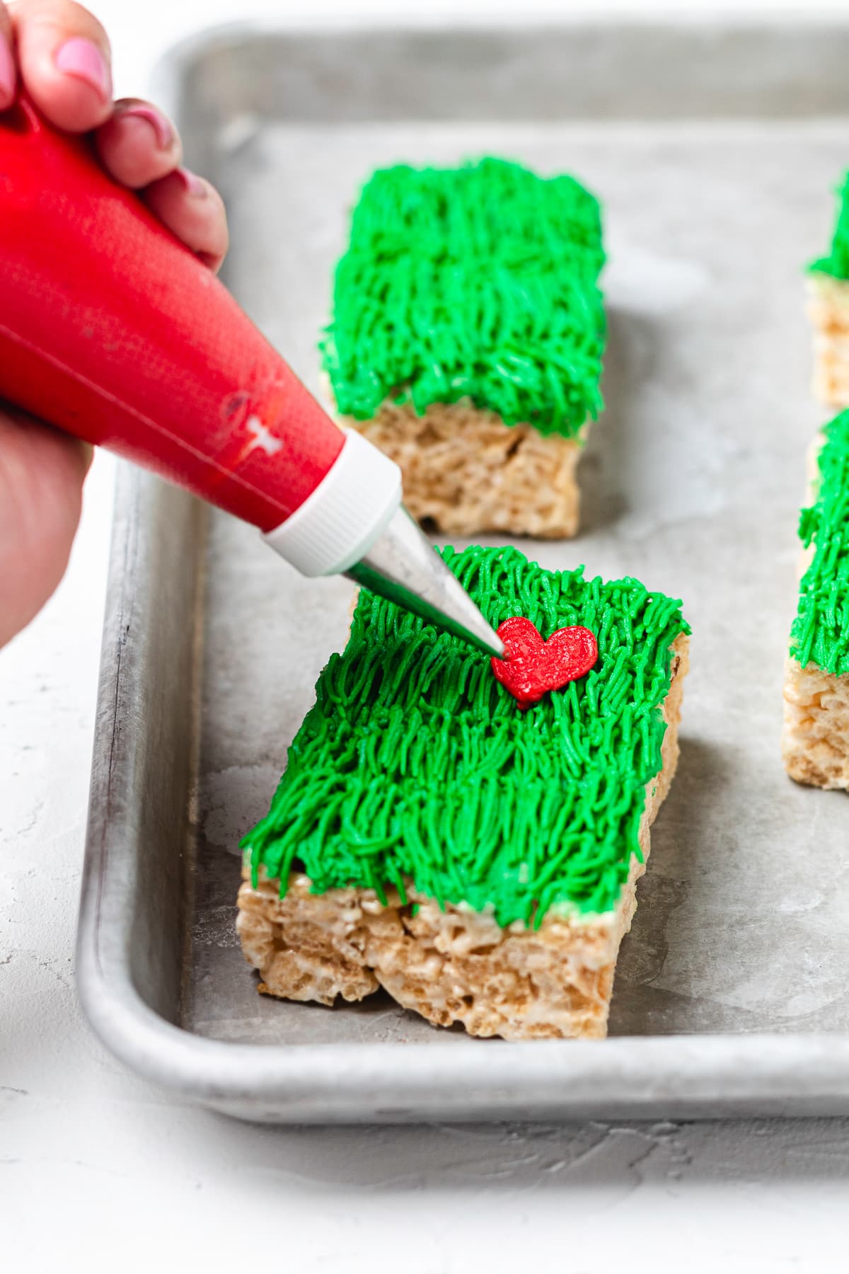 Piping a red heart onto a Grinch Rice Krispie treat.